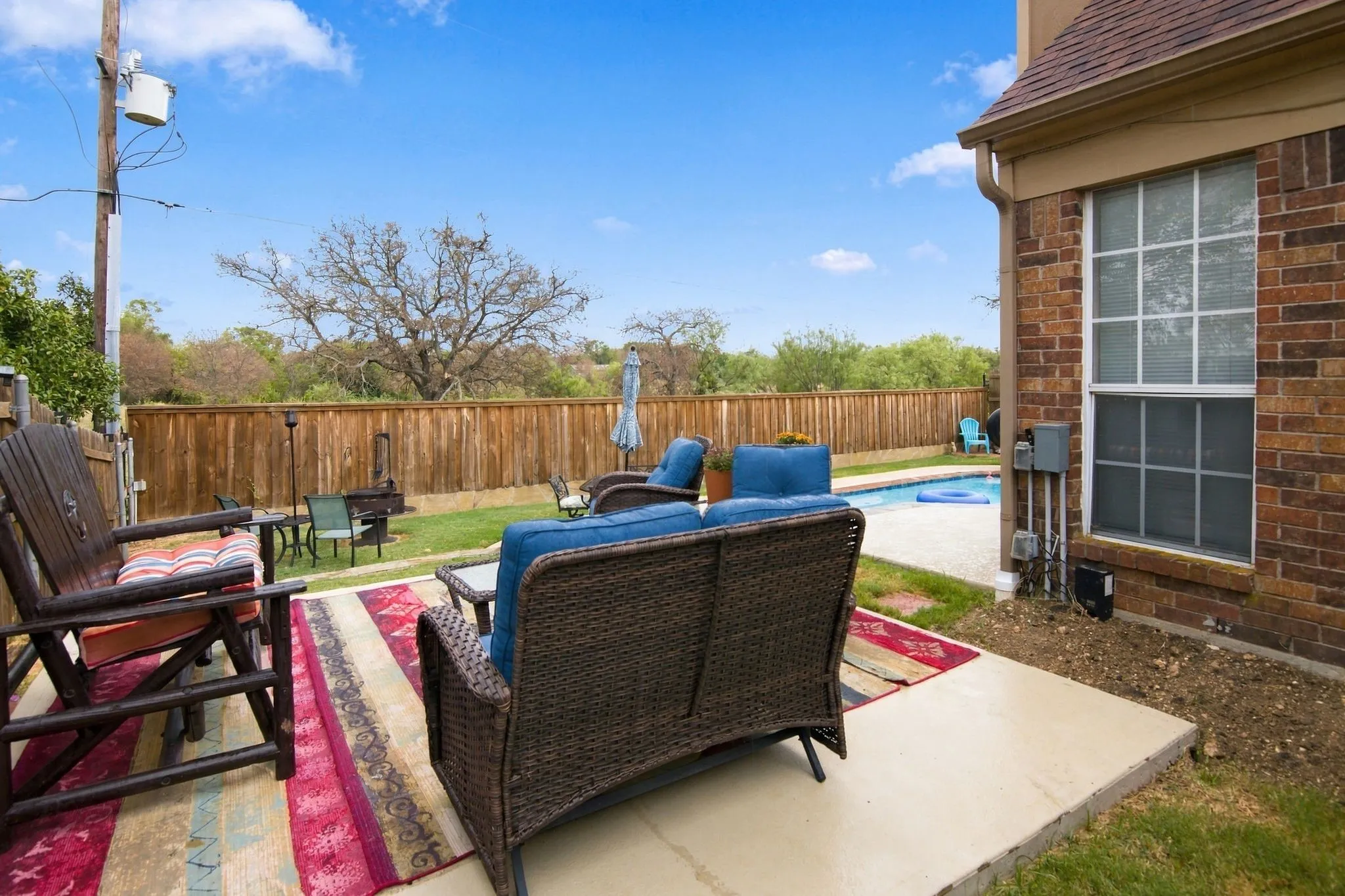 Expansive backyard featuring a privacy fence, concrete patio, inground pool, and a brick exterior with a large window