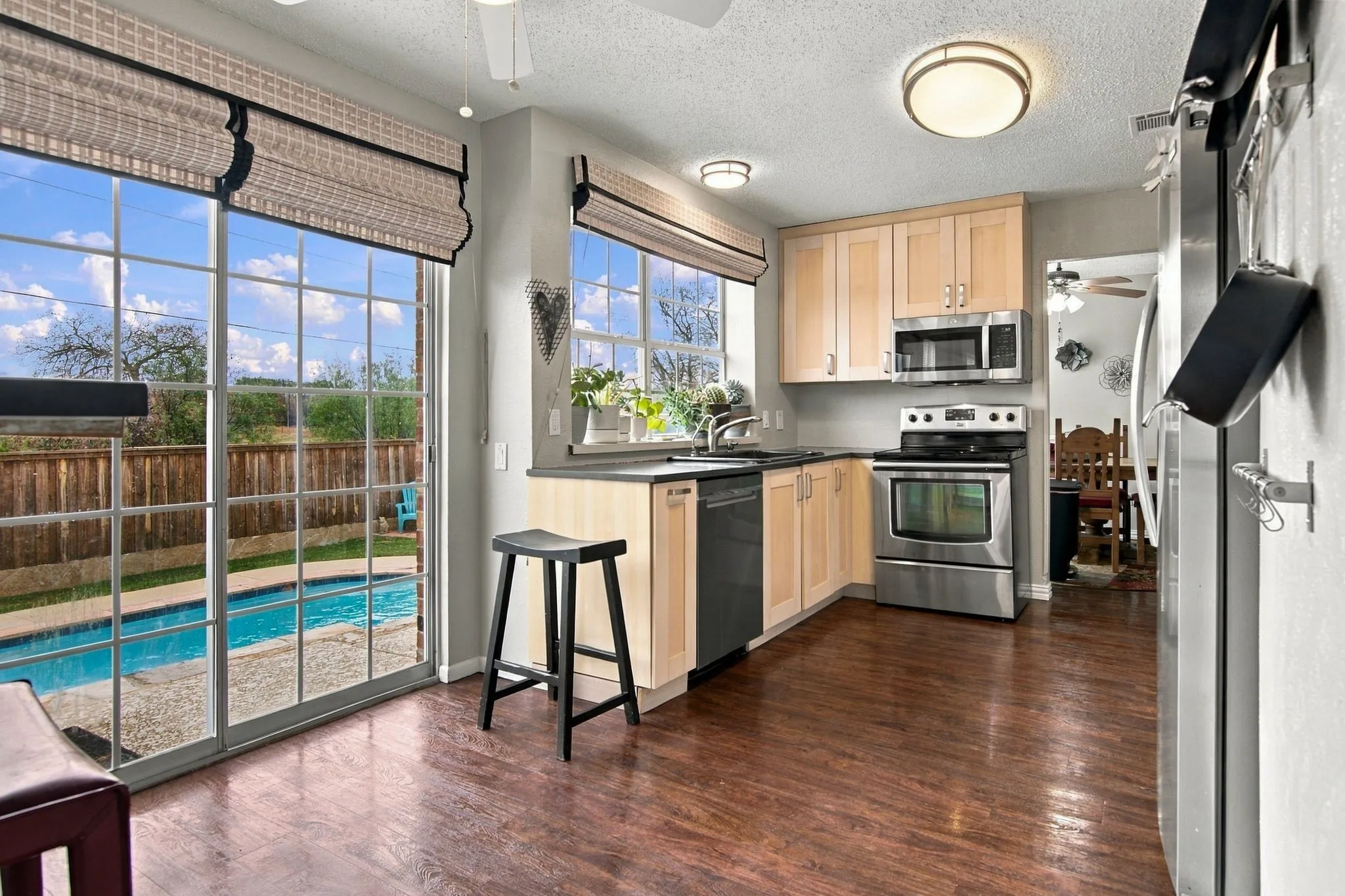 Kitchen with wood-finish flooring, light wood cabinetry, stainless steel appliances, and black countertops