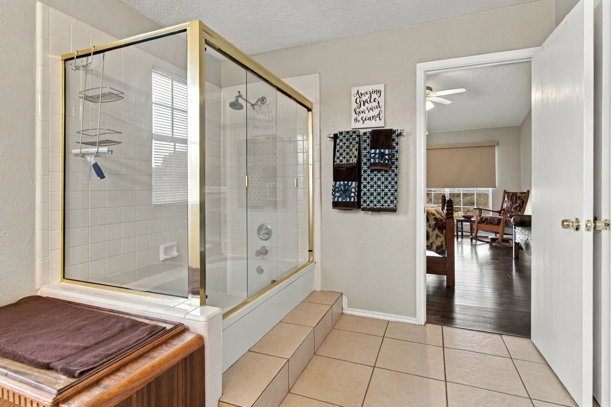 Tub/shower combination with a gold-finish glass enclosure, white tile surround, and an integrated step