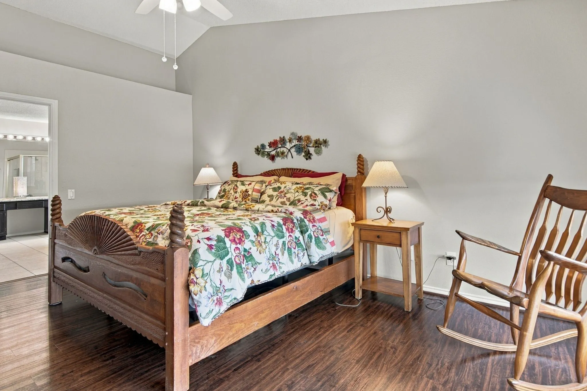 Vaulted ceiling with a ceiling fan, wood-finish flooring, and a doorway opening to a bathroom with tile flooring and a dual vanity