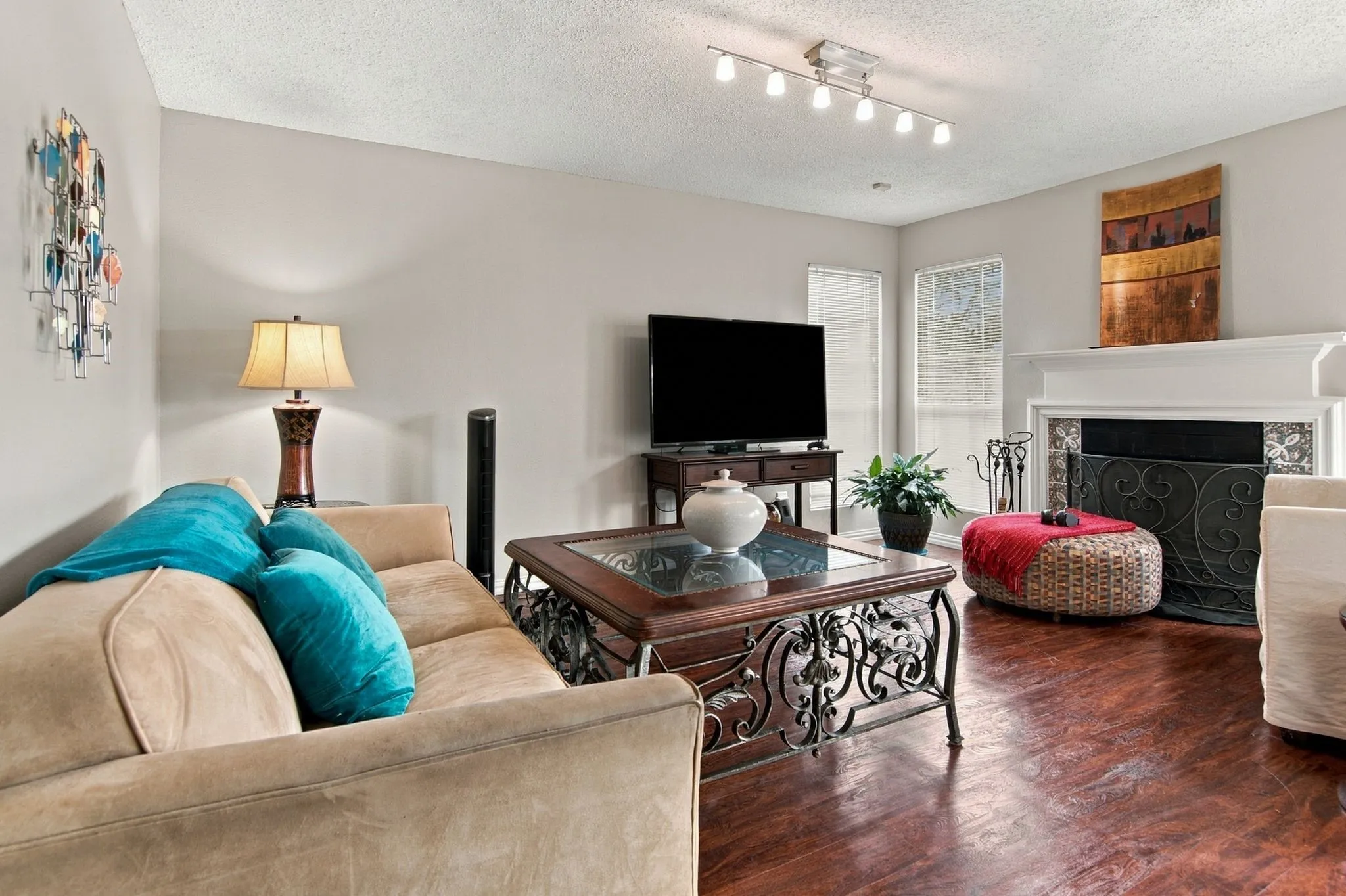 Hardwood-style flooring, white fireplace mantel, decorative fireplace screen, track lighting fixture, and multiple windows