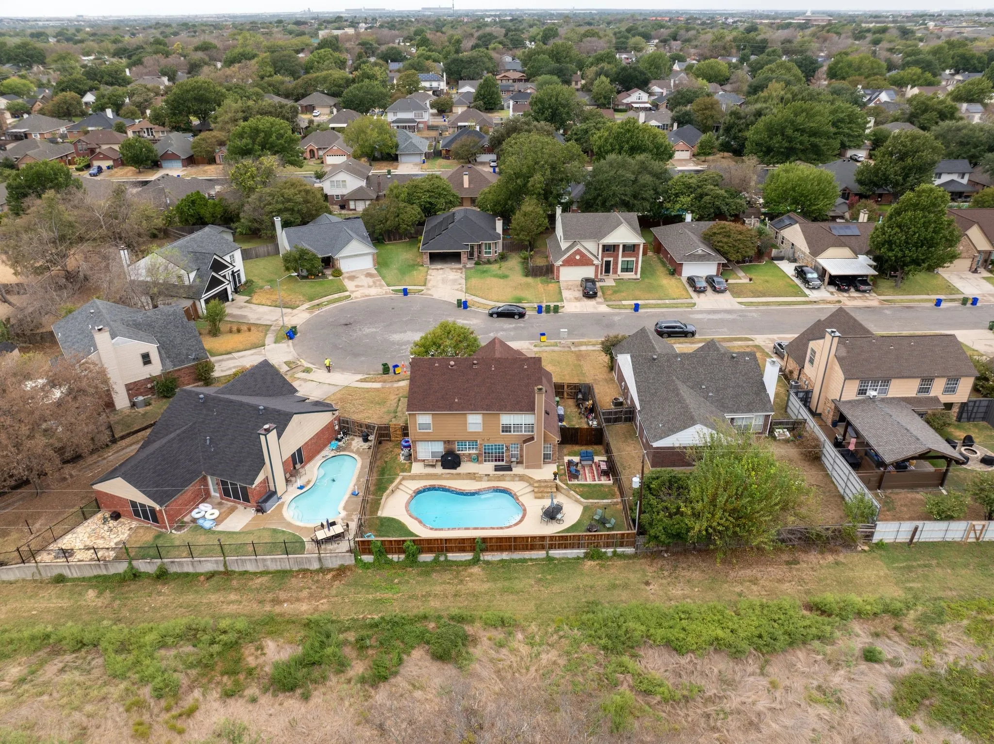 Aerial perspective of a residential neighborhood featuring cul-de-sac streets, mature trees, and multiple properties with private swimming pools