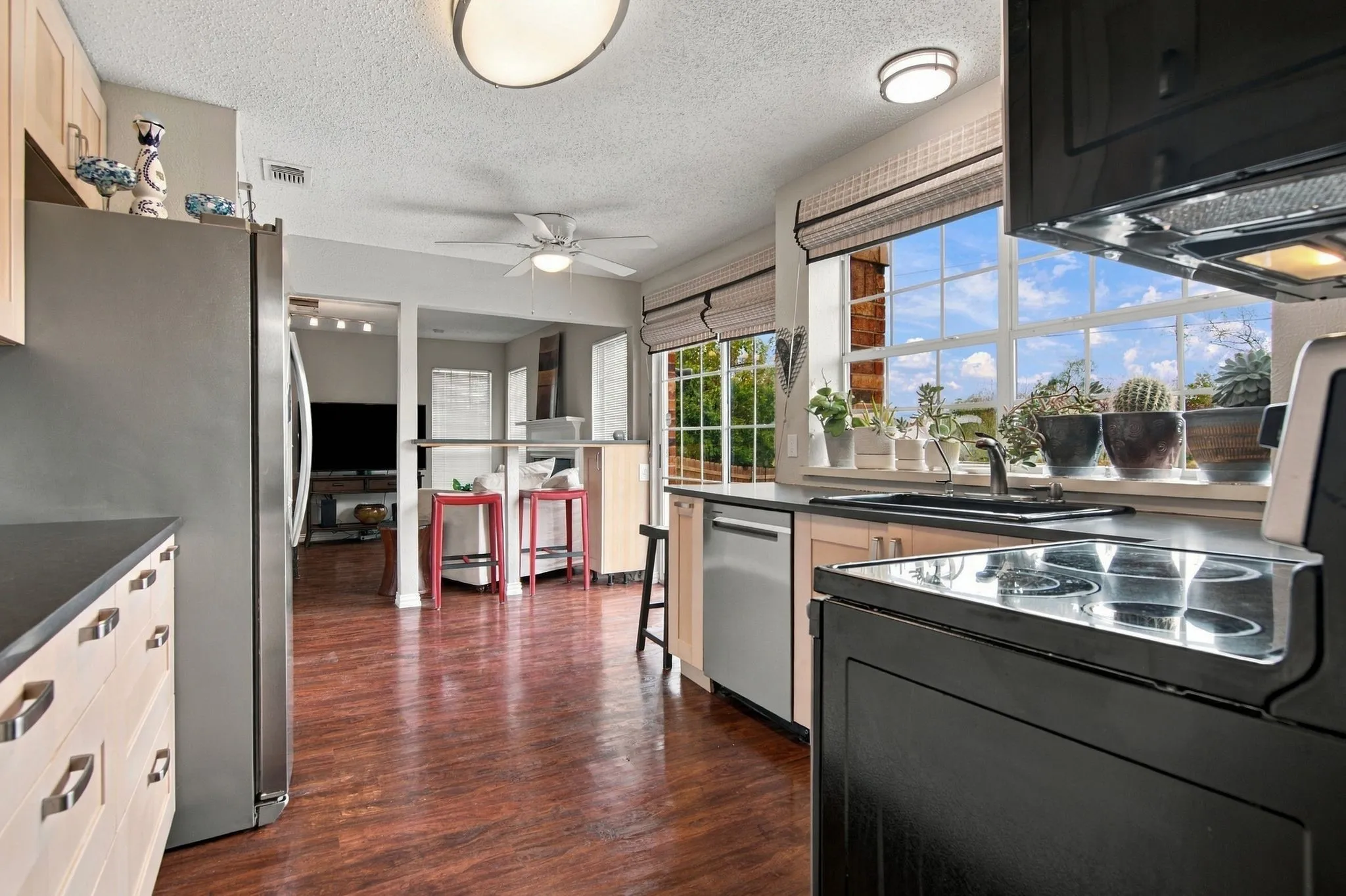 Kitchen featuring wood like flooring, light wood cabinetry, stainless steel appliances, and a built-in breakfast bar