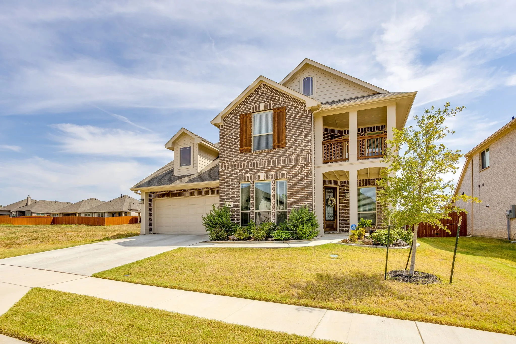 Brick and siding exterior with wood-finish shutters, an attached garage, and a two-story covered entry