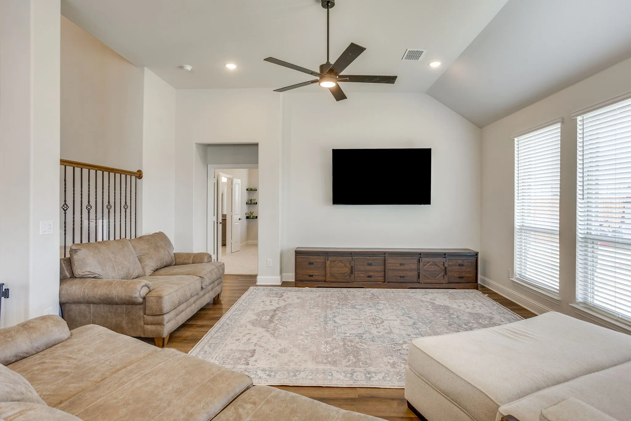 Vaulted ceiling with a ceiling fan and recessed lighting, wood-finish flooring, and two large windows with blinds