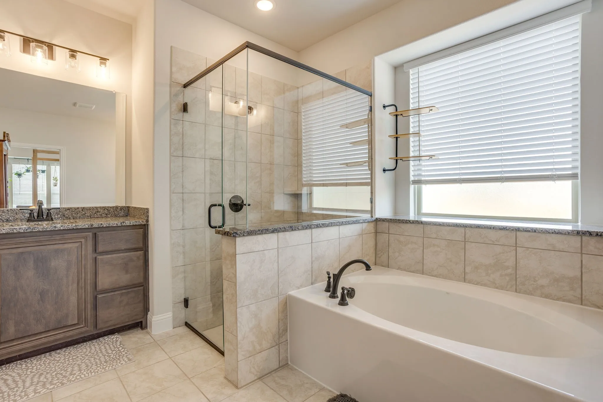 Bathroom featuring a large soaking tub, walk-in shower with glass enclosure, single vanity with wood-finish cabinetry and stone countertop, and tiled flooring