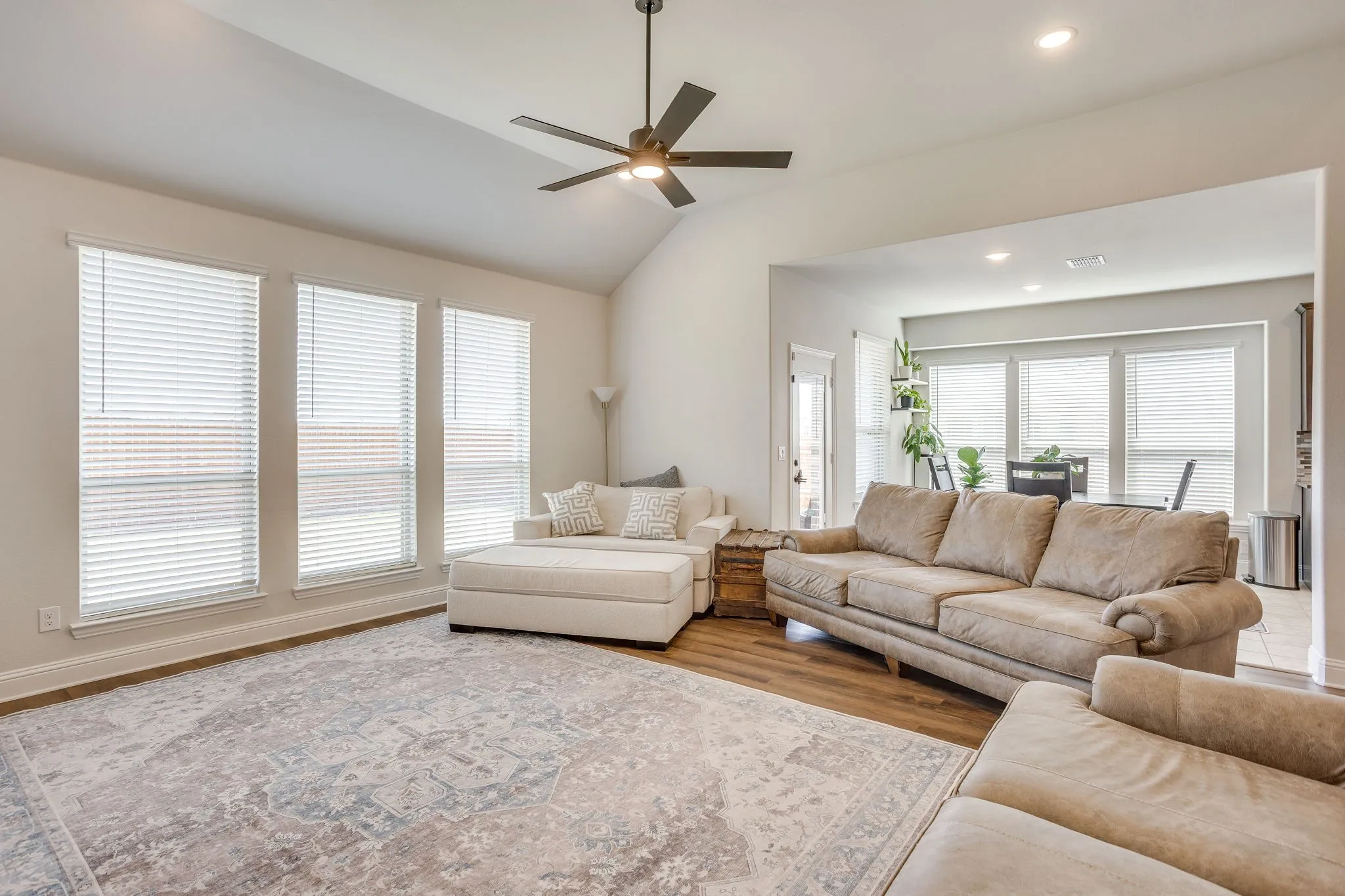 Vaulted ceiling, wood-finish flooring, recessed lighting, ceiling fan, and multiple windows with blinds