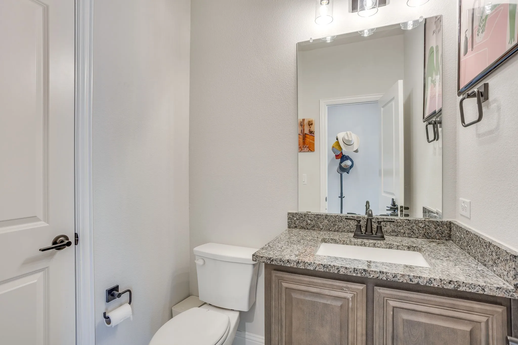 White paneled door with dark hardware, built-in vanity with a granite countertop, undermount sink, dark-finish faucet, and a large wall-mounted mirror