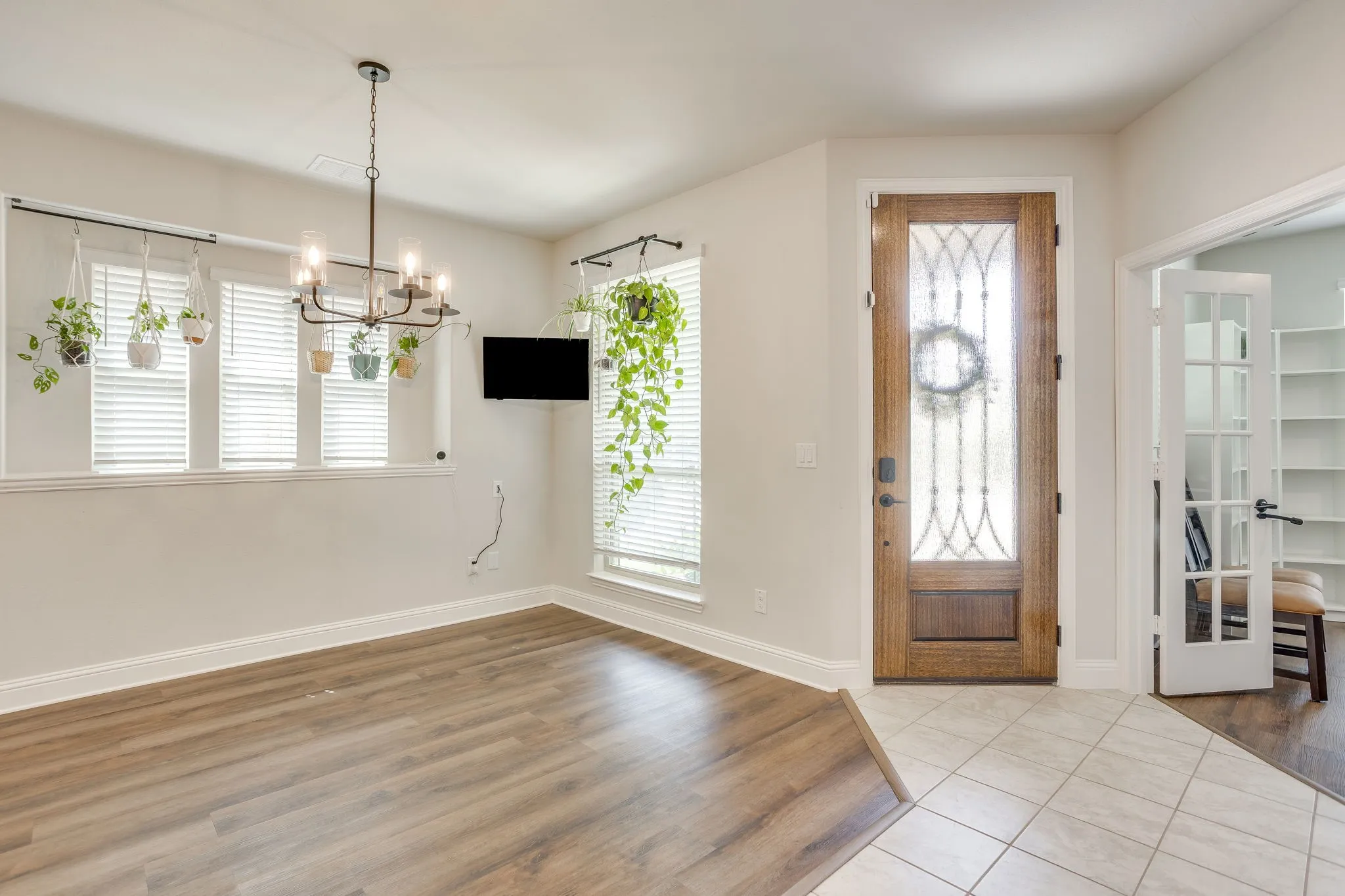 Wood-finish flooring, tiled entry, decorative glass front door, modern chandelier, and French doors