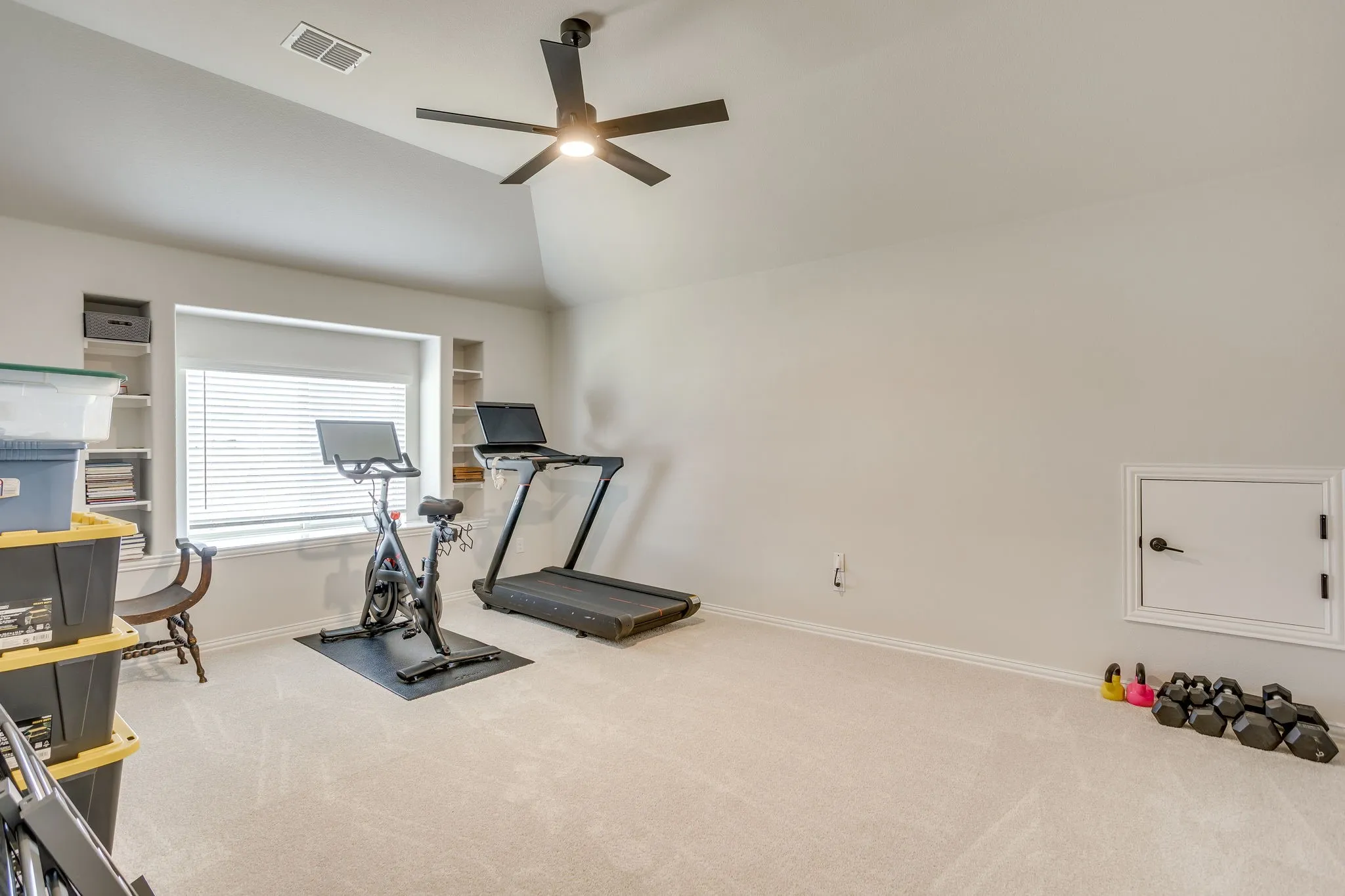 Carpeted room featuring a ceiling fan, recessed window with blinds, and built-in shelving