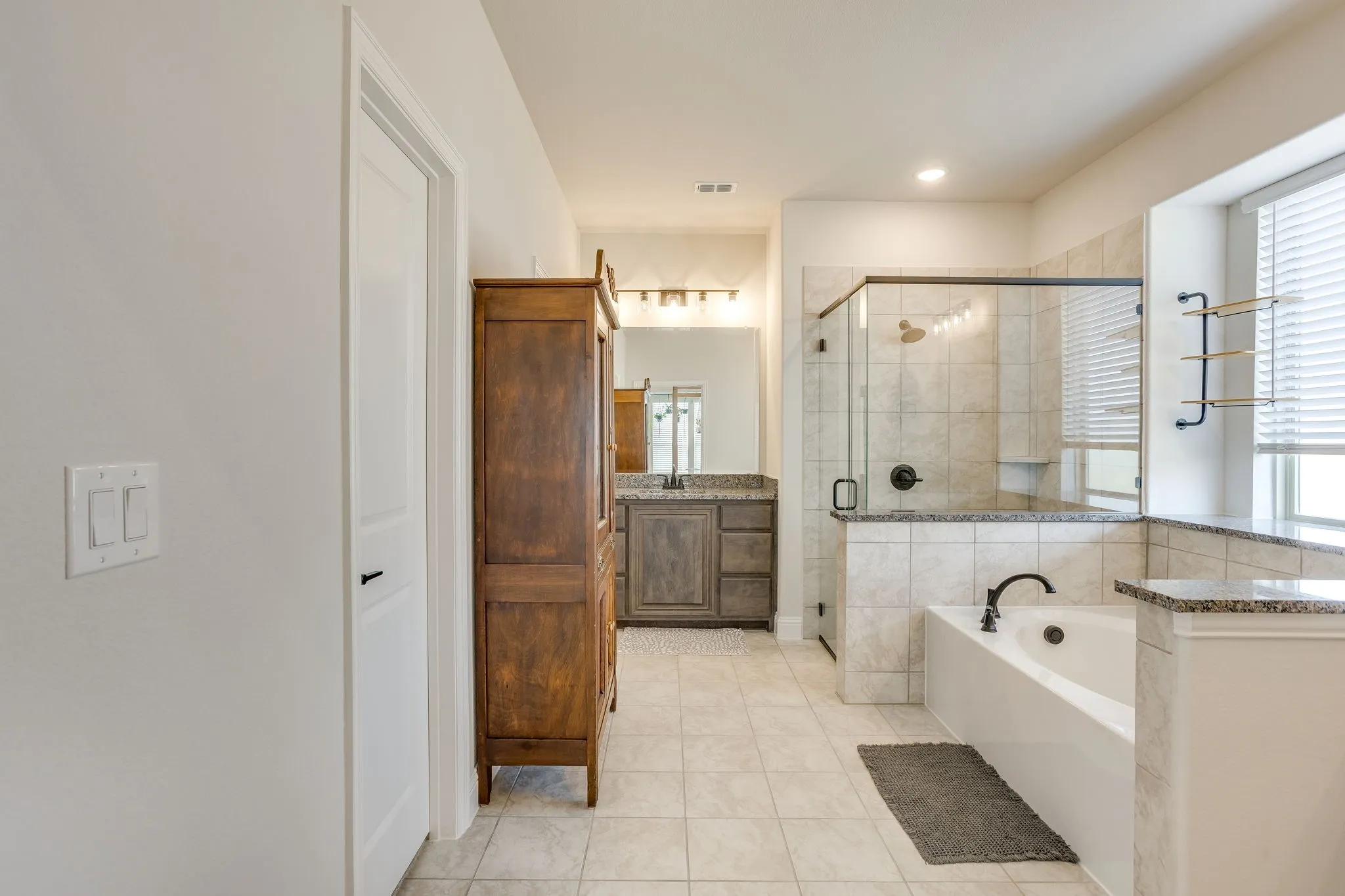 Bathroom featuring a built-in soaking tub, glass-enclosed shower, tiled flooring, and dual vanity with dark cabinetry