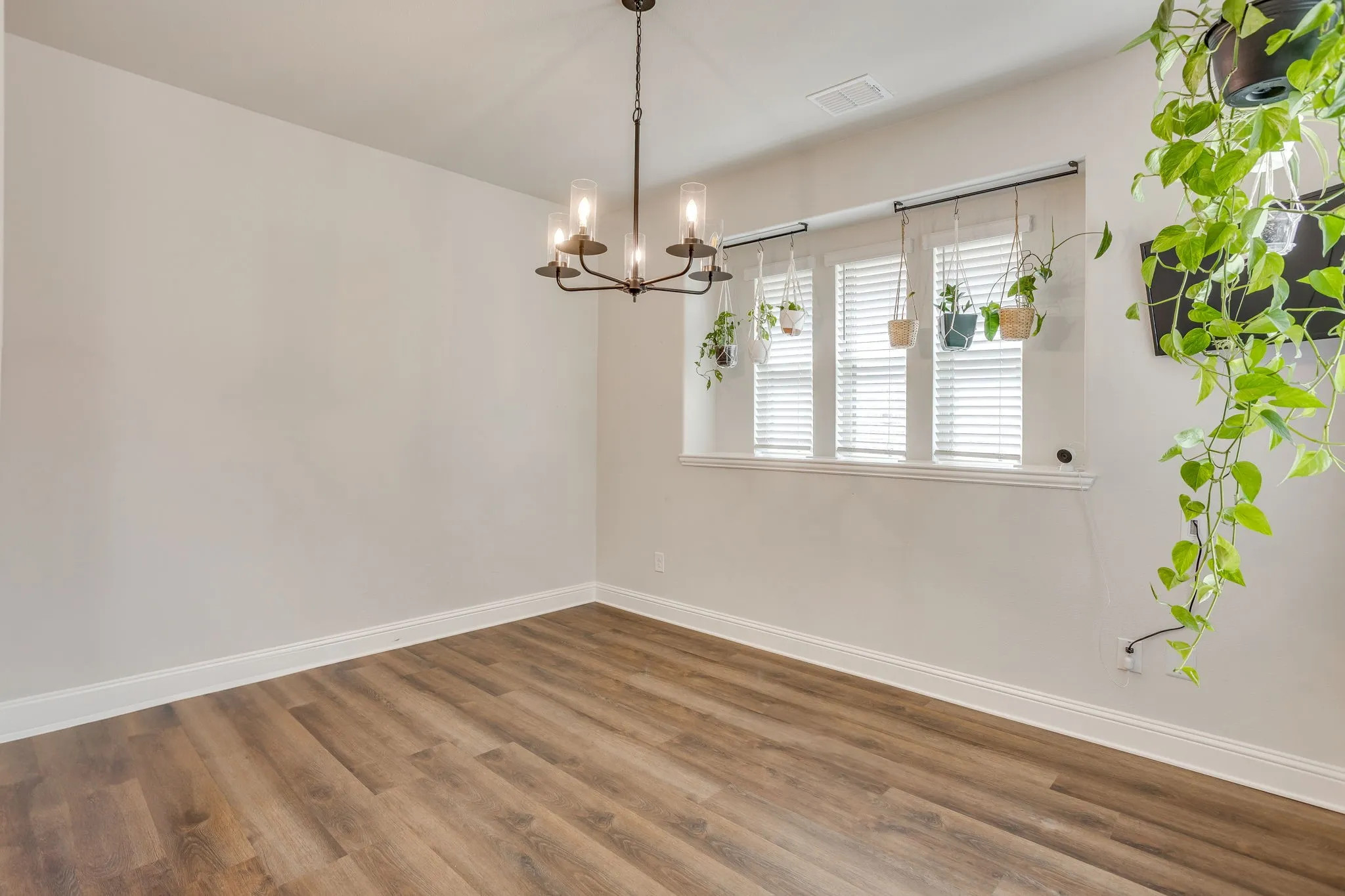 Wood-finish flooring with white baseboards, a multi-pane window with white blinds, and a dark-toned chandelier