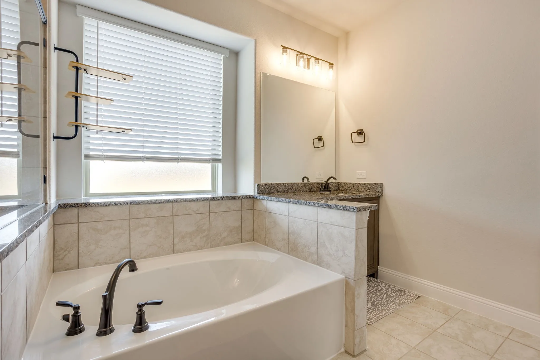 Built-in soaking tub with dark bronze fixtures, tile surround, and an adjacent vanity featuring a granite-style countertop