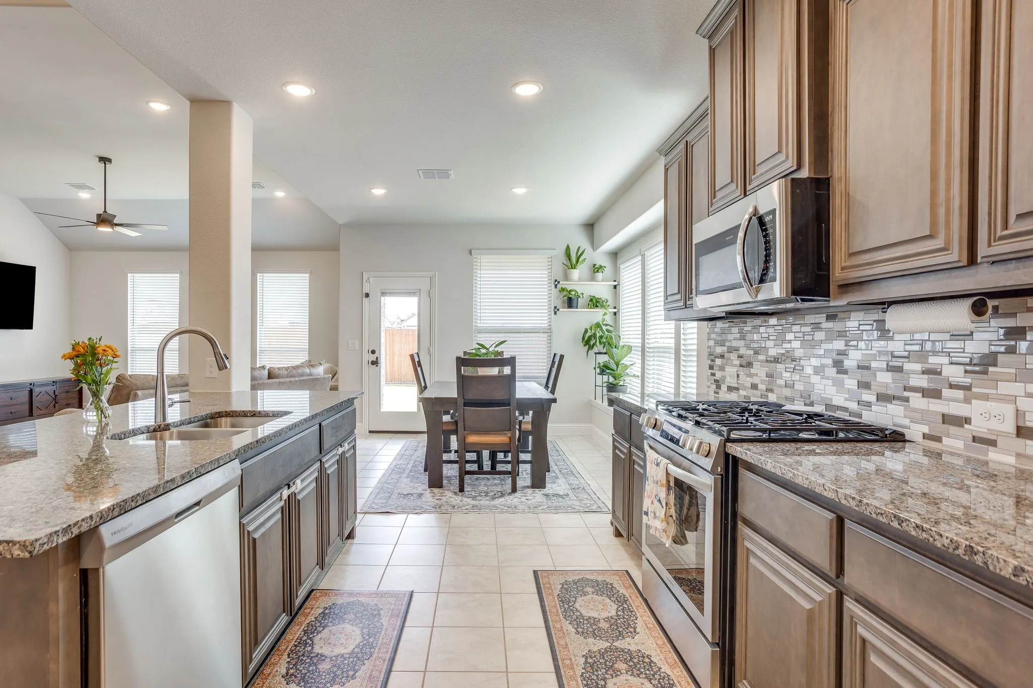 Kitchen featuring granite countertops, stainless steel appliances, wood cabinetry, tile flooring, and a mosaic tile backsplash