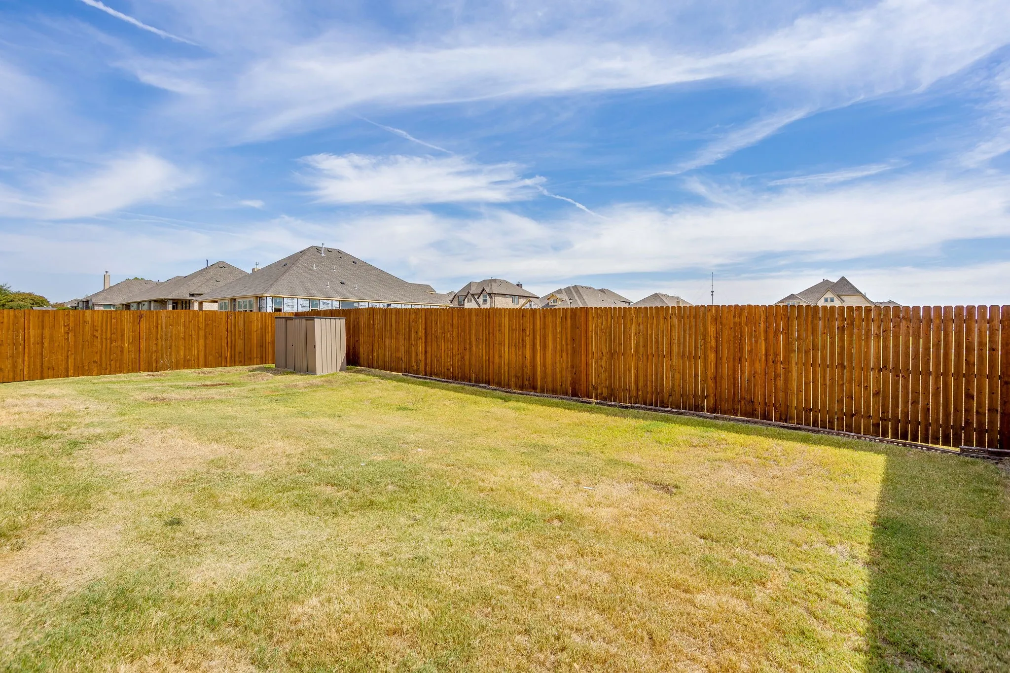 Expansive backyard featuring a natural wood privacy fence, a storage shed, and a broad grassy area