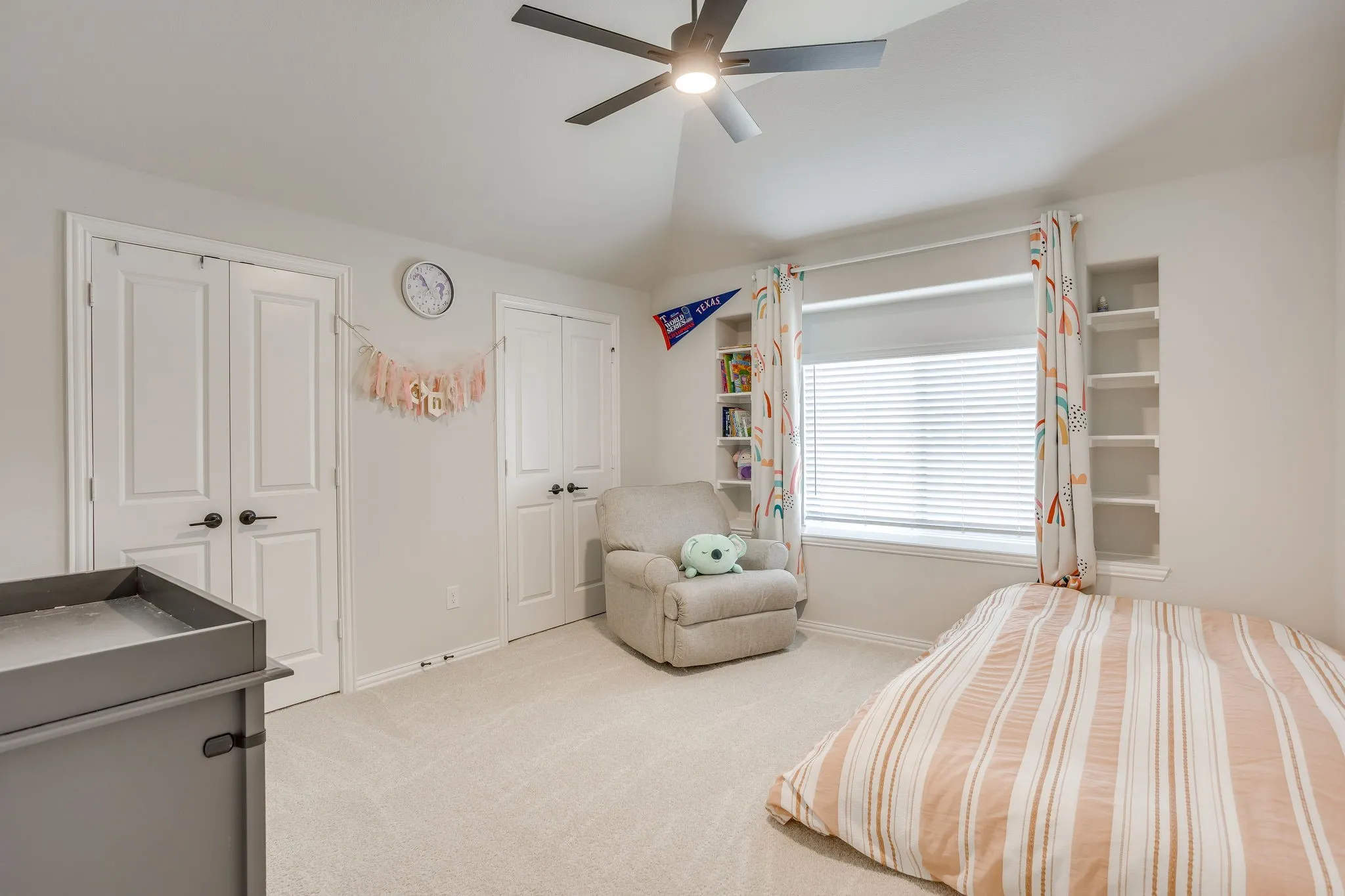 Recessed built-in shelving, window with blinds, ceiling fan with integrated lighting, two panel doors, and neutral carpet flooring