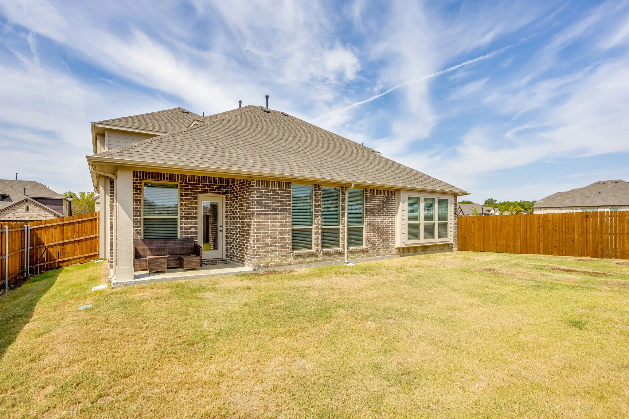 Brick exterior with multiple windows, covered patio, and a shingle roof