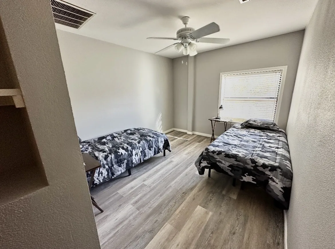 Room with wood-finish flooring, a ceiling fan with integrated lighting, and a window with horizontal blinds
