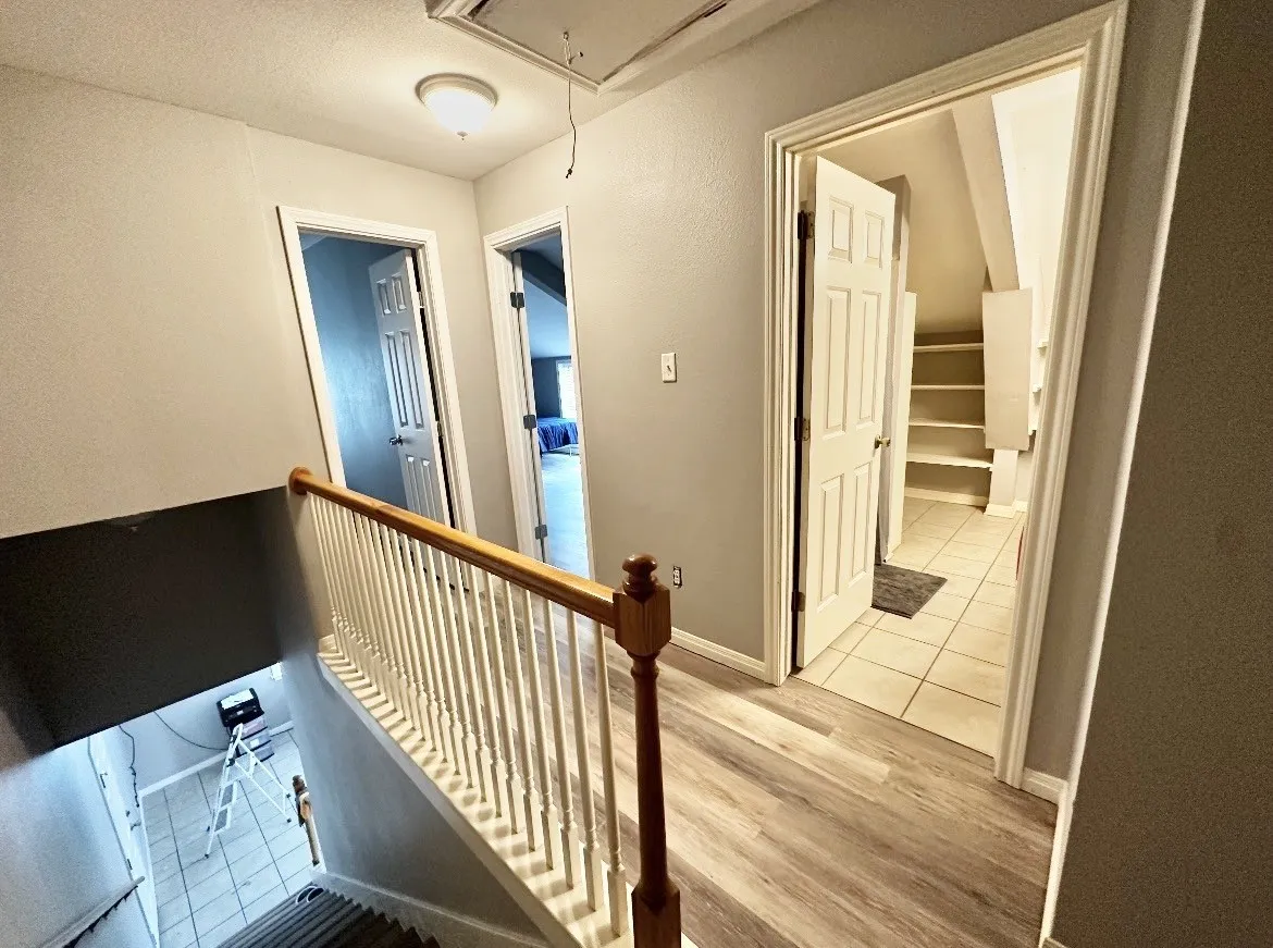 Wood-finish flooring, white panel doors, and a wood handrail with white spindles