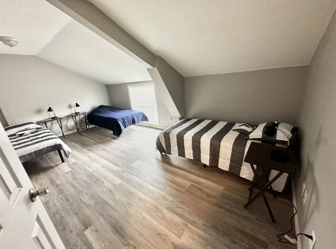 Sloped ceiling room featuring wood-finish flooring, a window with horizontal blinds, and neutral wall tones