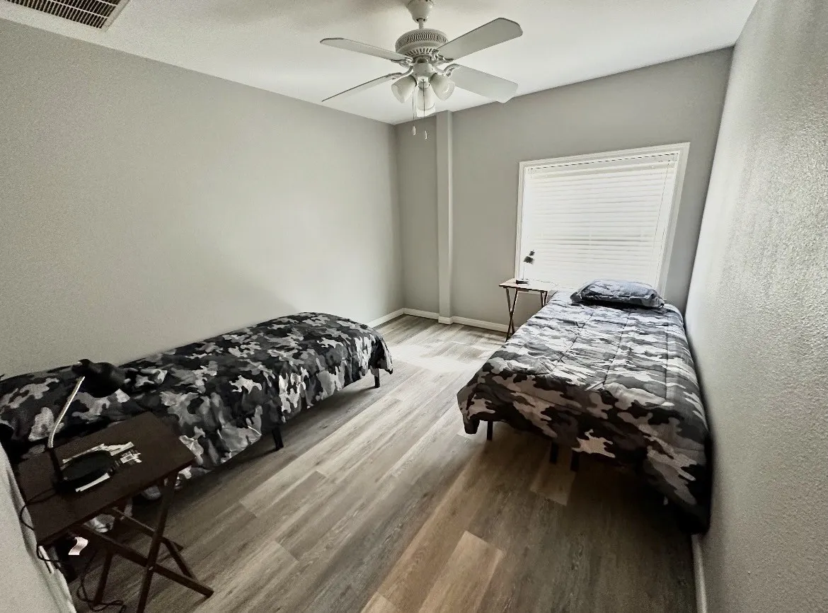 Wood-finish flooring, ceiling fan, window with horizontal blinds, and neutral wall color