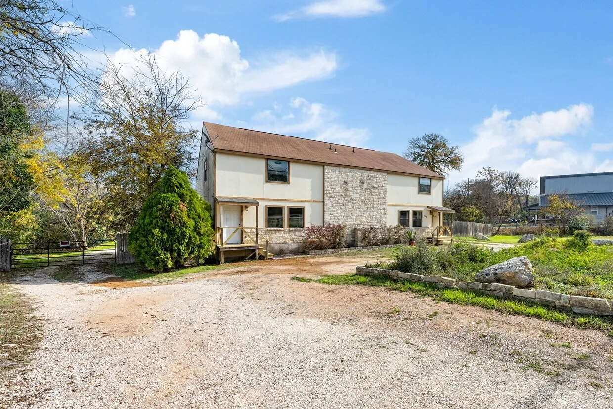 Two-story exterior with stone and siding facade, covered entryways, and a gravel drive