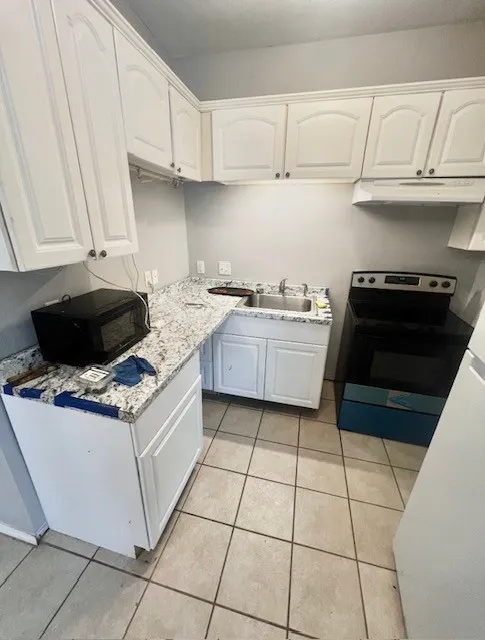 White cabinetry with polished hardware, granite-style countertops, stainless steel sink, built-in range hood, and tile flooring