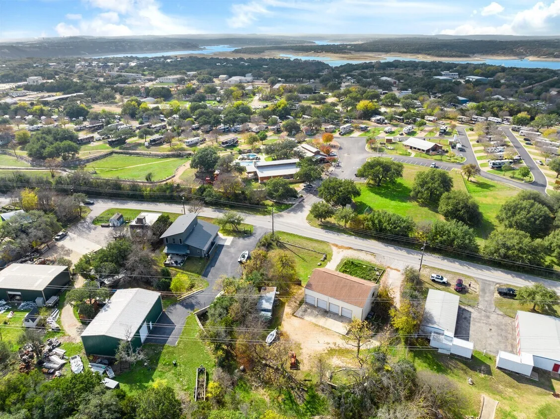 Expansive property featuring multiple structures, paved roads, established trees, and distant water