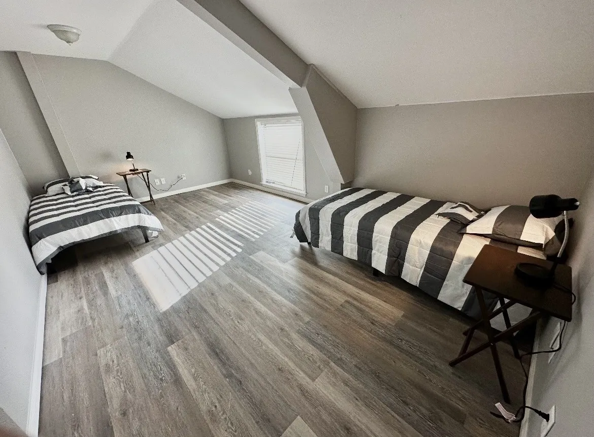 Sloped ceilings, wood-finish flooring, and a window with blinds