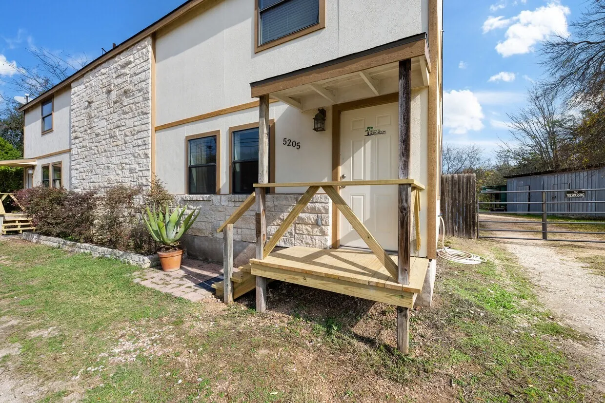Stucco and stone facade with multiple windows, featuring a covered front entry porch with wood railing and steps