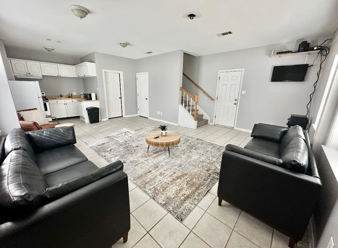 Open-concept common area featuring tile flooring, white kitchen cabinetry, and a staircase with wood handrails