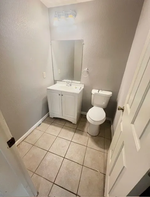 White vanity with integrated sink, rectangular mirror, and neutral tile flooring