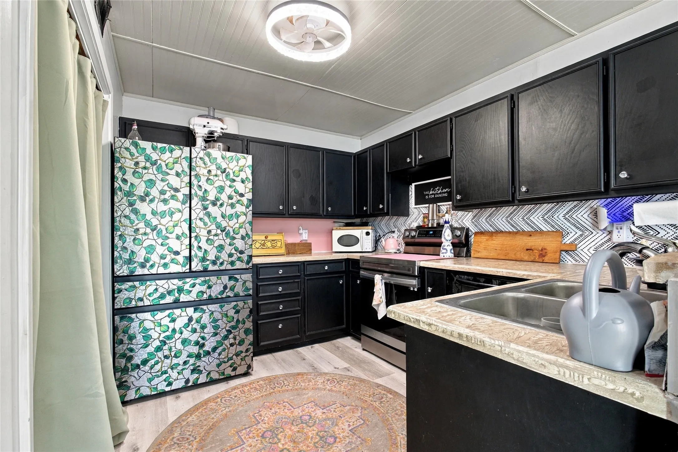 Kitchen featuring black cabinetry, light wood-finish flooring, a stainless steel double basin sink, and a decorative backsplash