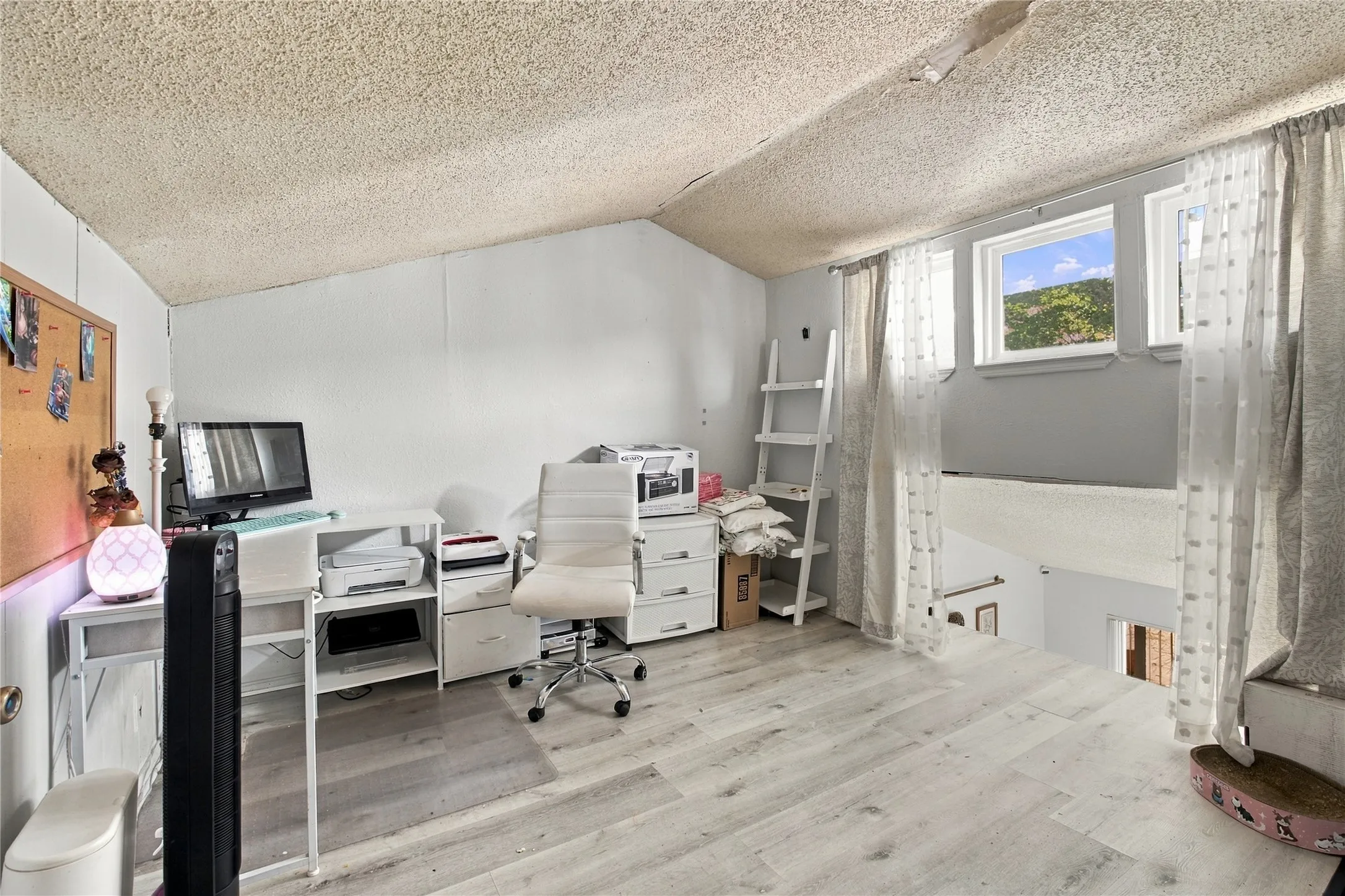 Vaulted ceiling with textured finish, wood-finish flooring, multiple windows, and a built-in ladder