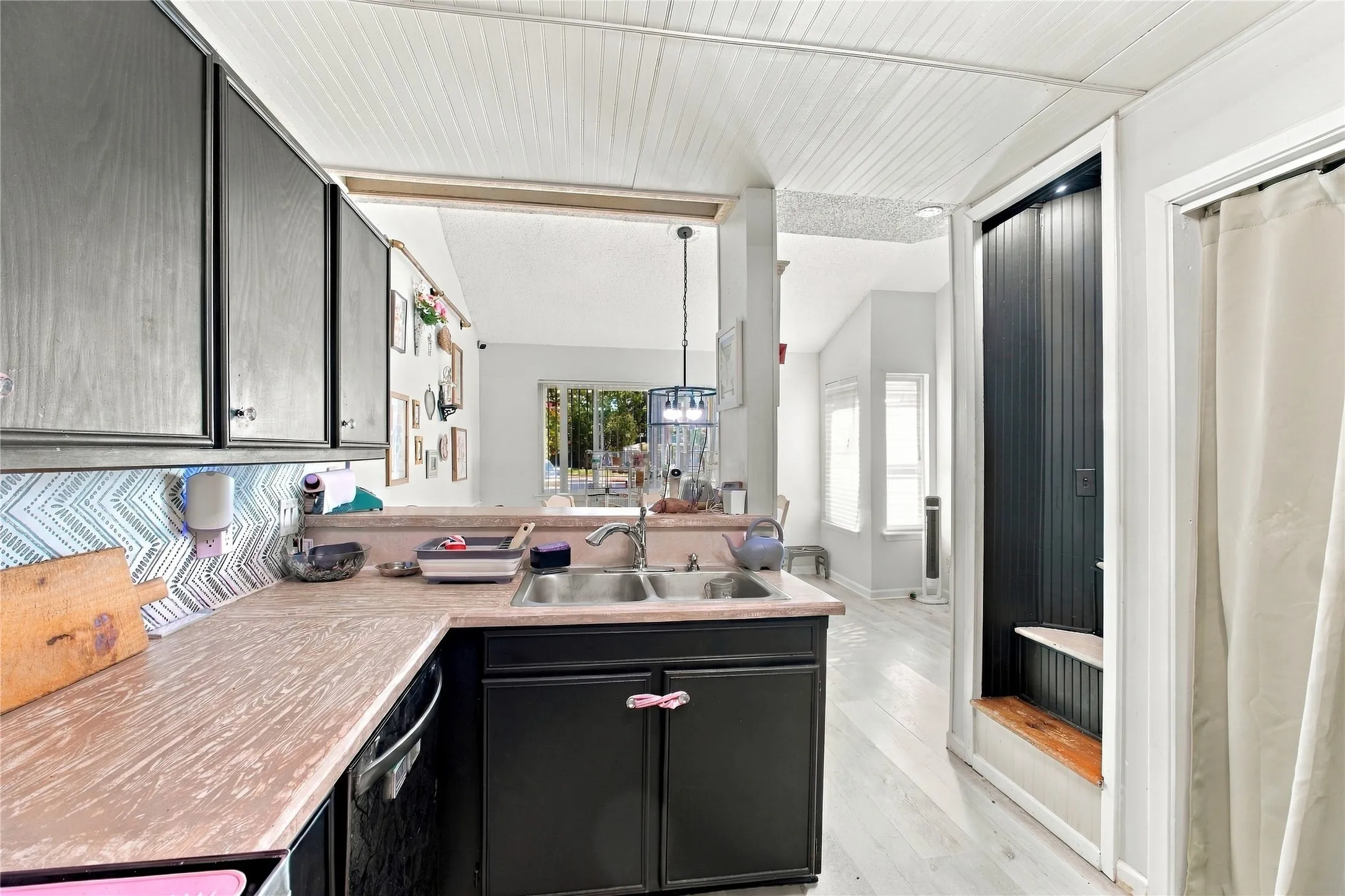 Kitchen featuring dark cabinetry, dual basin sink, patterned backsplash, and light wood-finish flooring
