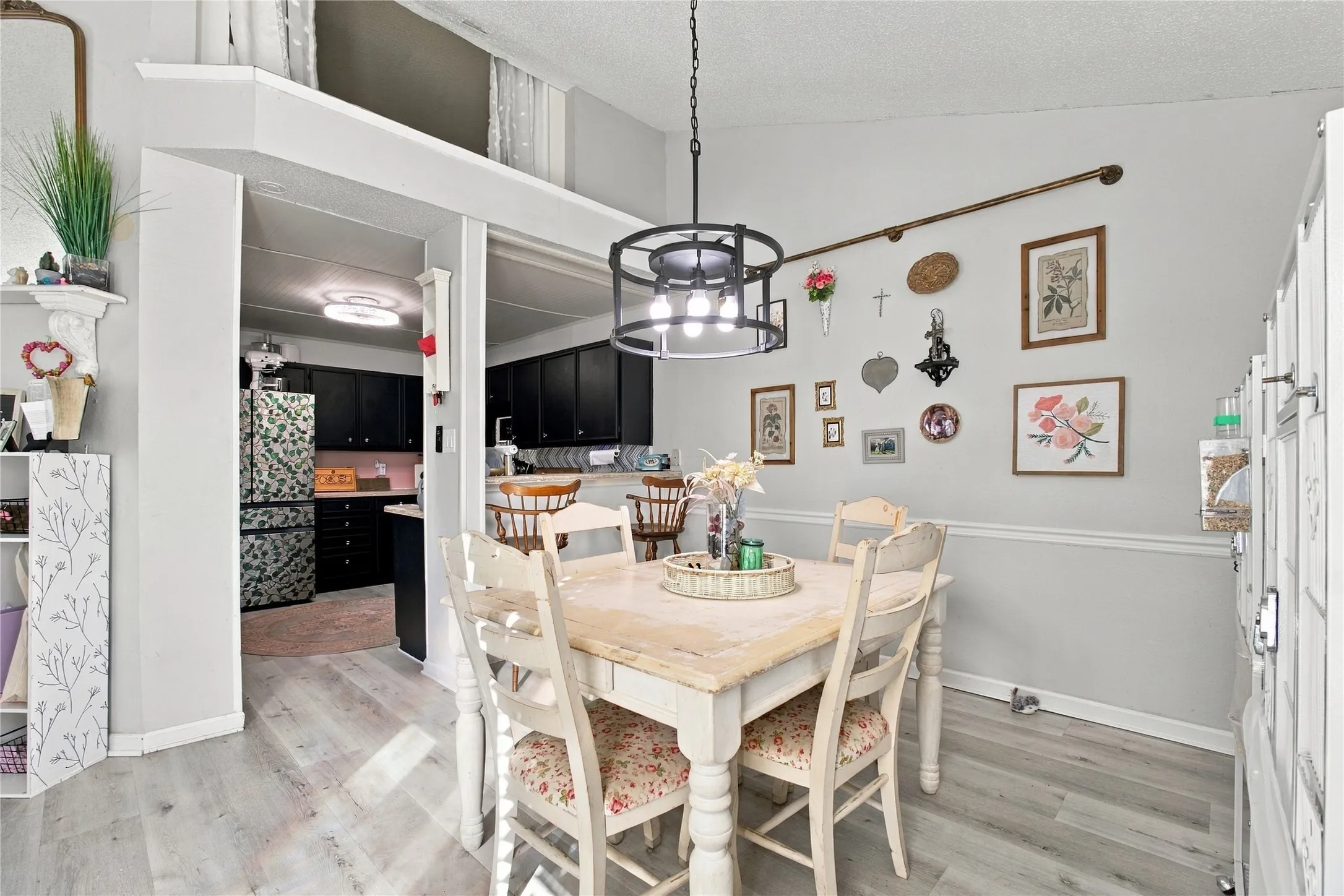 Vaulted ceiling with a contemporary chandelier, light wood-finish flooring, and a cased opening to the kitchen featuring dark cabinetry