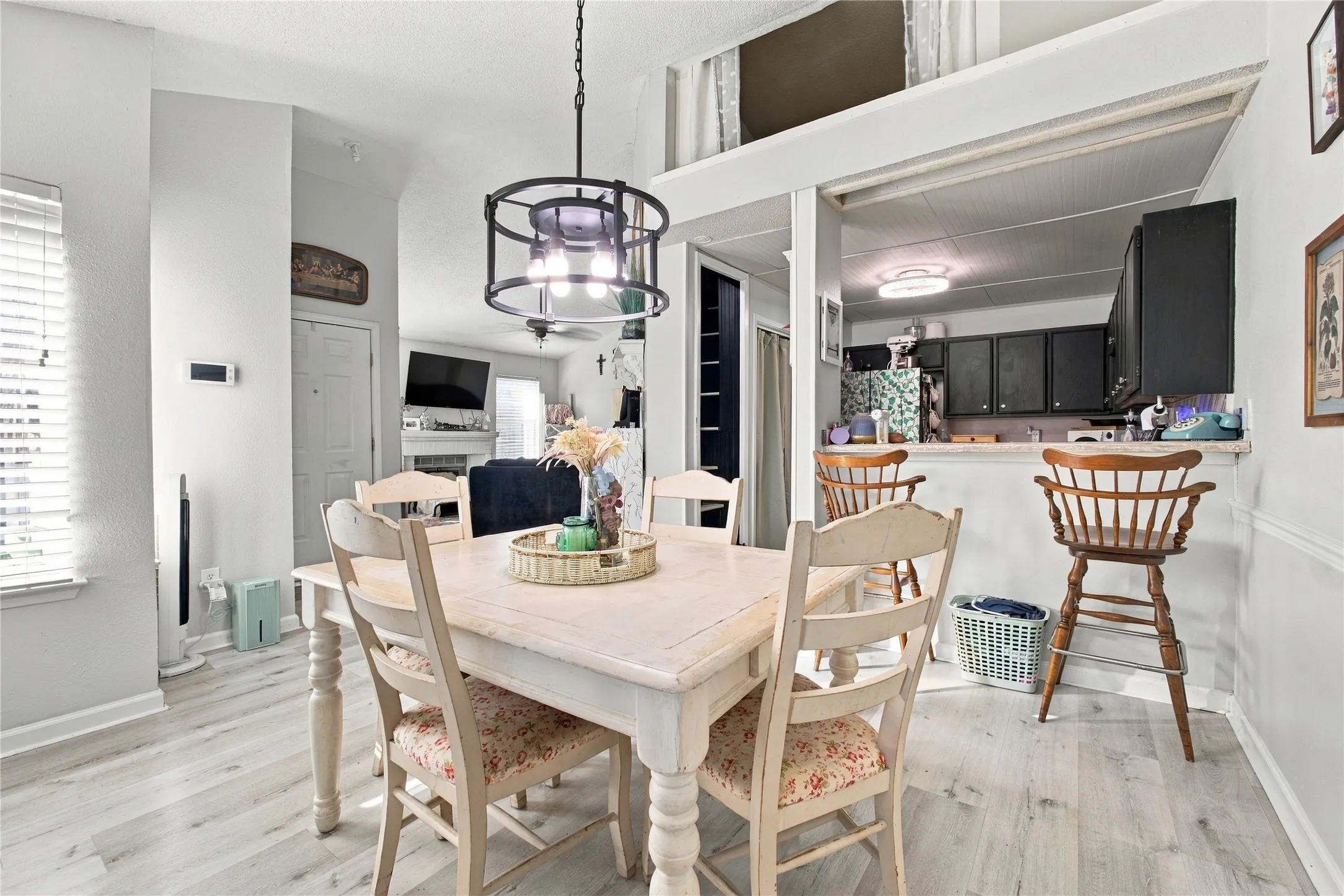 Light wood-finish flooring throughout, framed opening to the kitchen, black upper cabinetry, and a circular chandelier