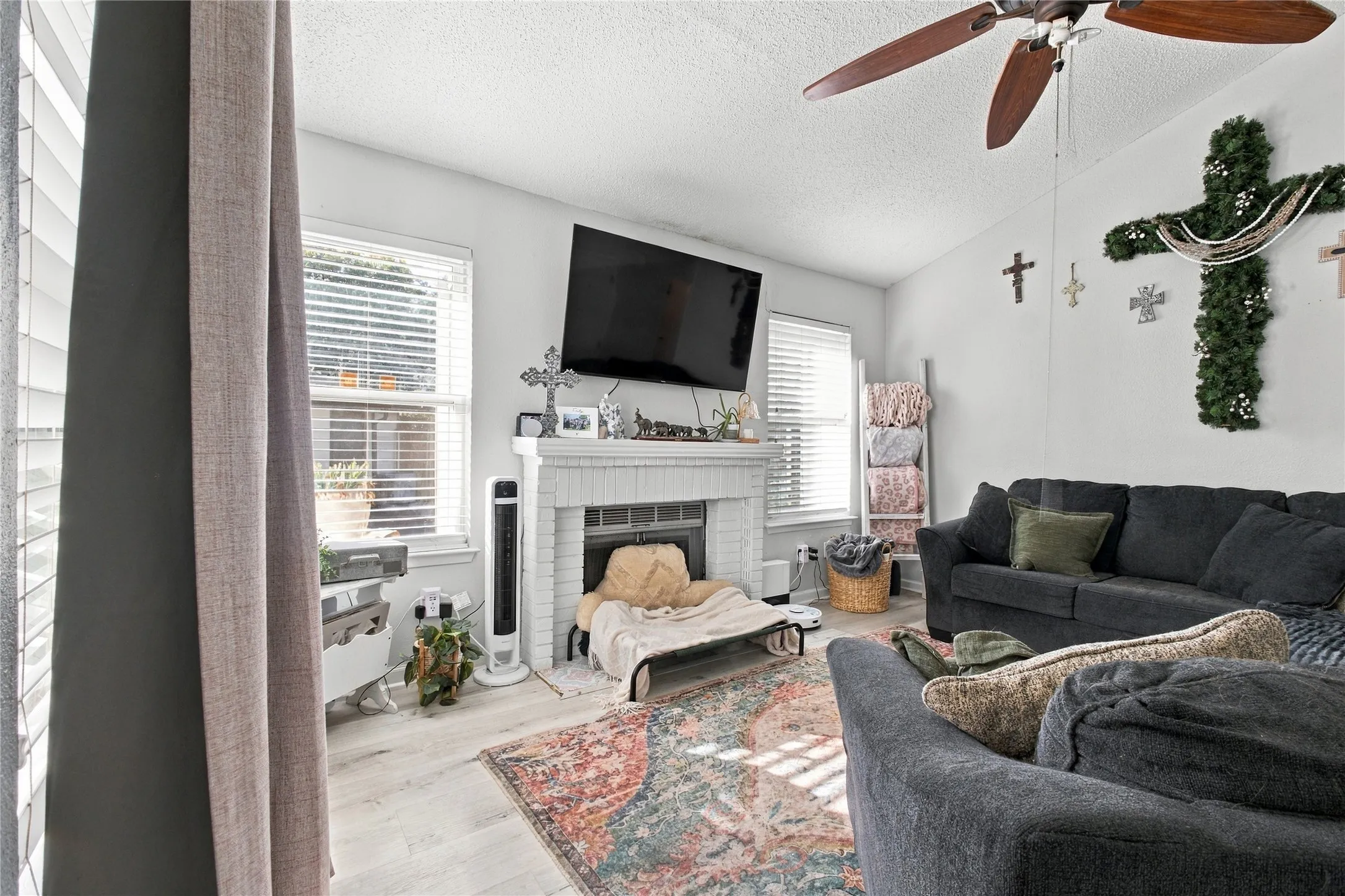 Vaulted ceiling with a ceiling fan, white fireplace, multiple windows with blinds, and light wood-finish flooring