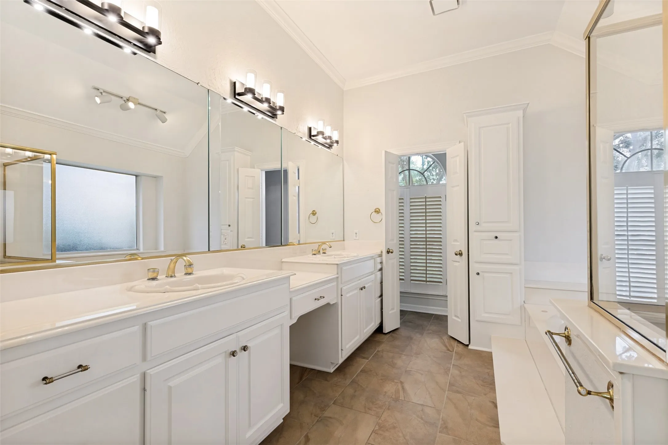 Bathroom featuring dual vanities with integrated sinks, white cabinetry, and extensive mirror coverage