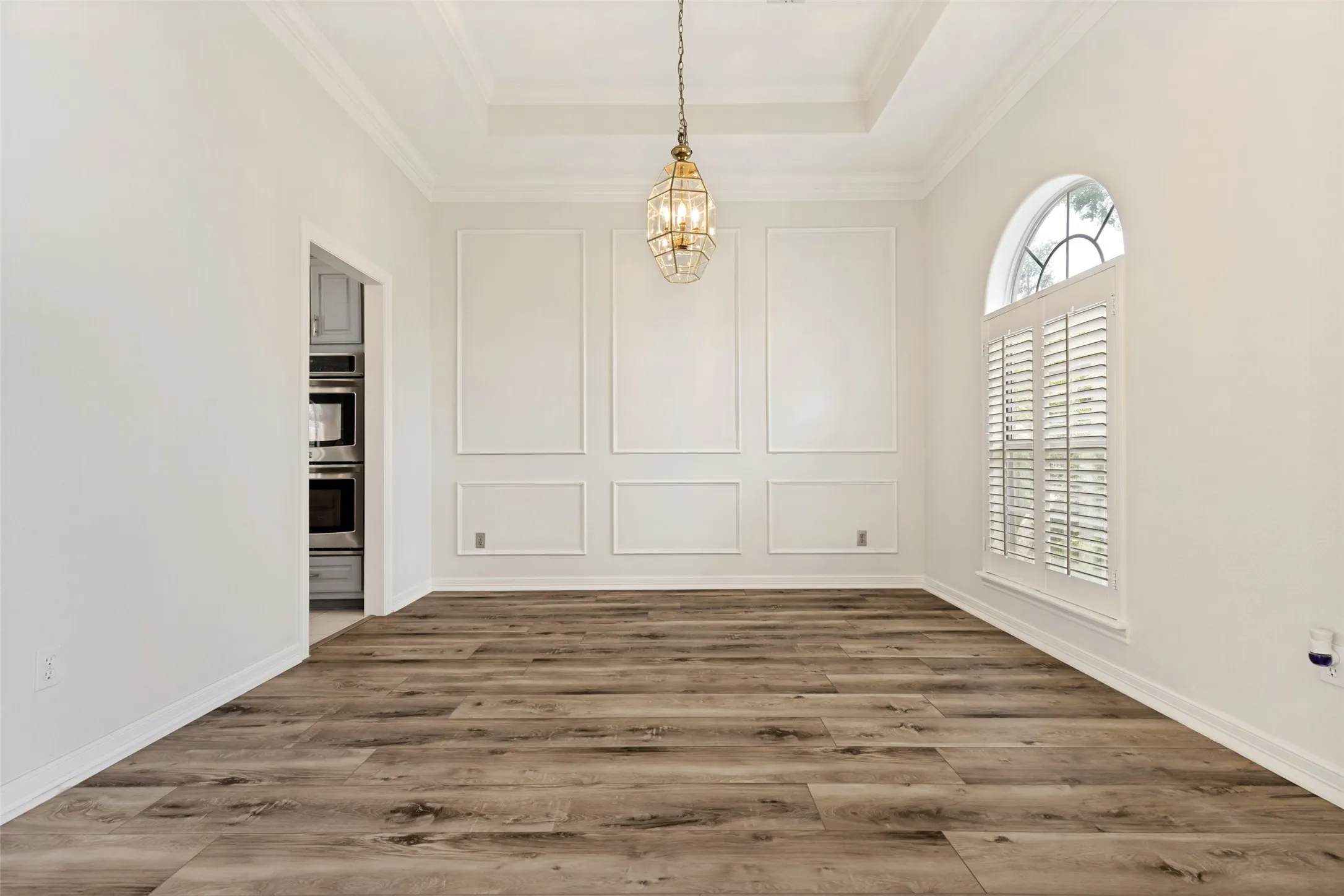 Spacious dining room featuring wood-finish flooring, decorative wall molding, and a tray ceiling with a suspended chandelier