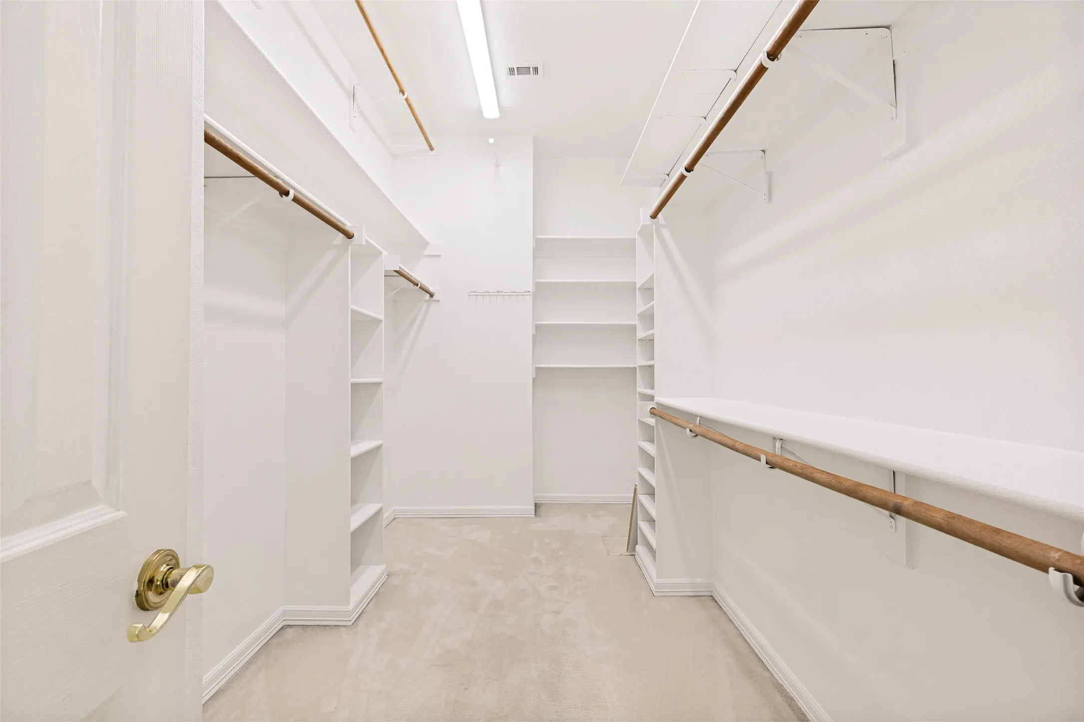 Spacious walk-in closet featuring light-colored carpeting, extensive built-in shelving, multiple hanging rods, and recessed lighting