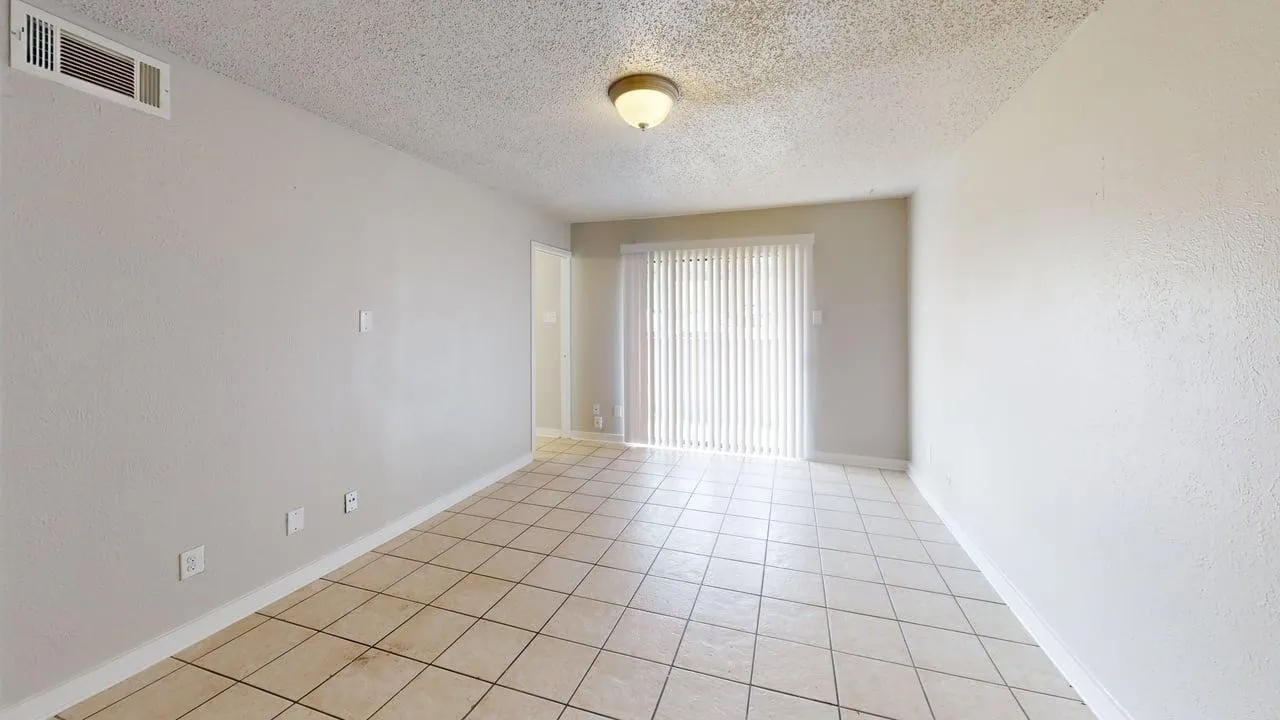 Neutral wall tones, tiled flooring, overhead lighting, and vertical blinds on sliding glass doors
