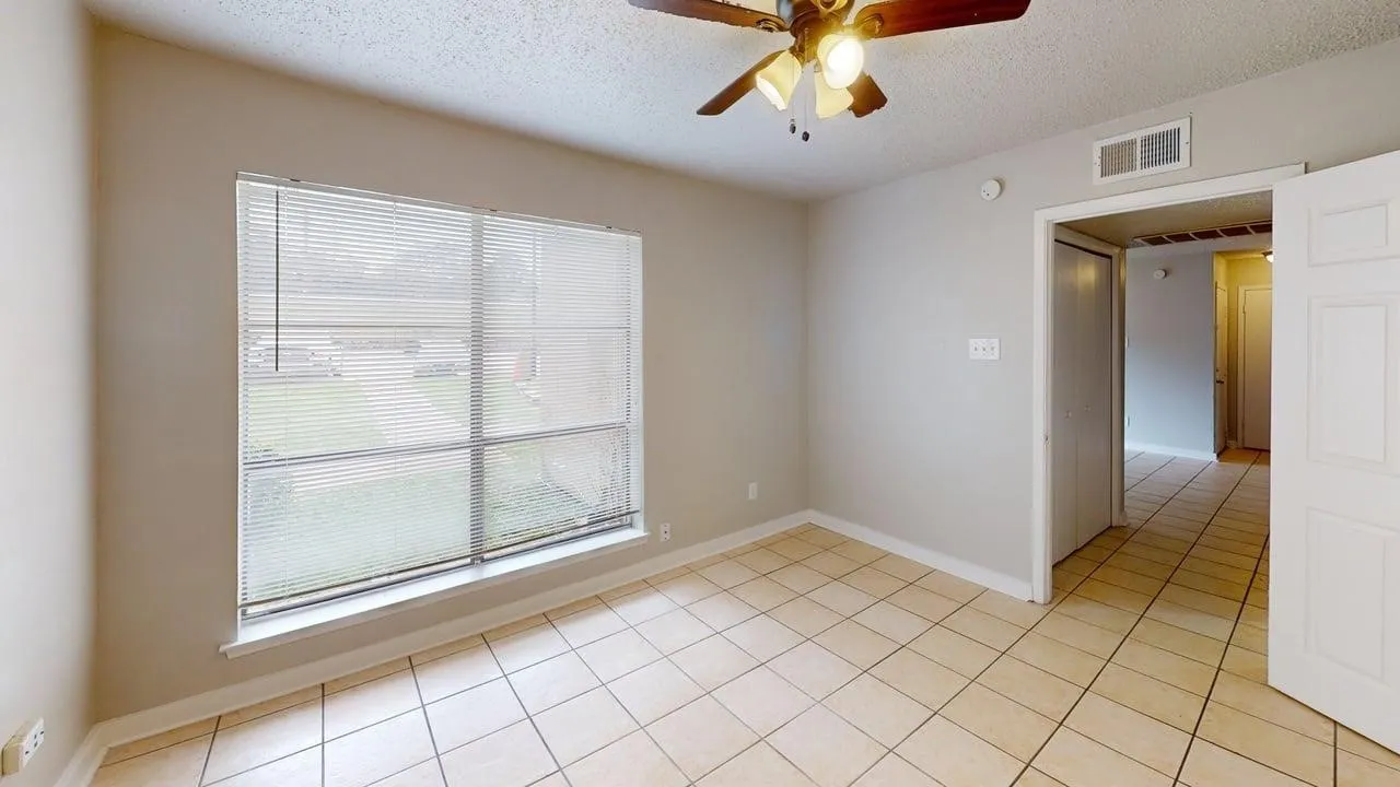 Light-toned tile flooring, neutral wall paint, and a large window with blinds
