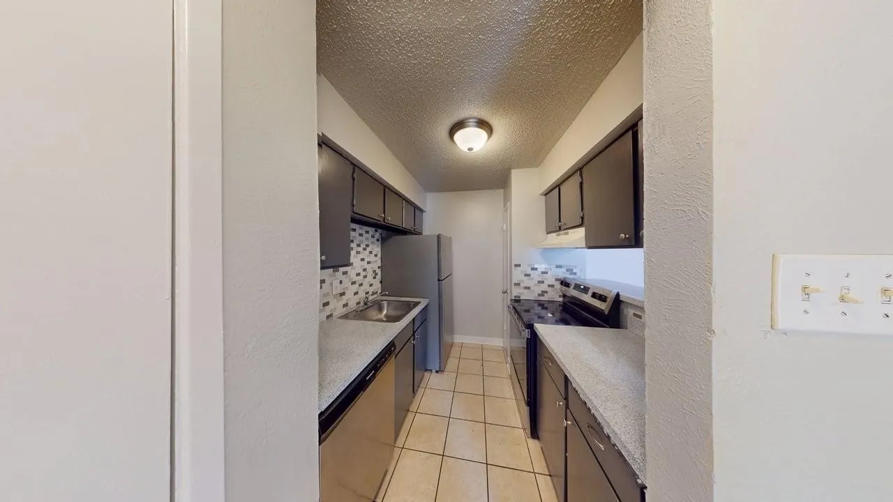 Galley kitchen featuring dark cabinetry, light countertops, a tile backsplash, and stainless steel appliances