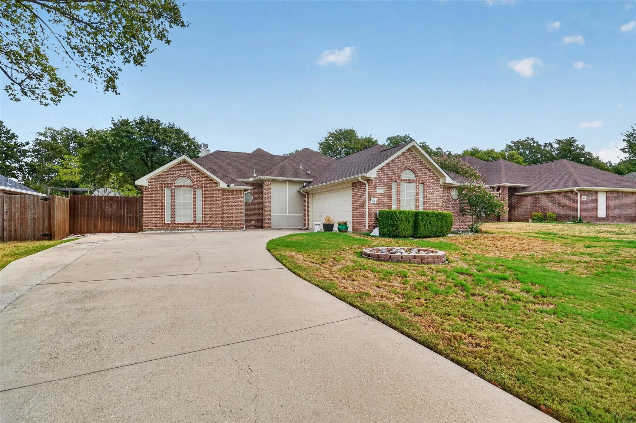 Brick exterior with arched window accents, mature trees, and an expansive concrete driveway