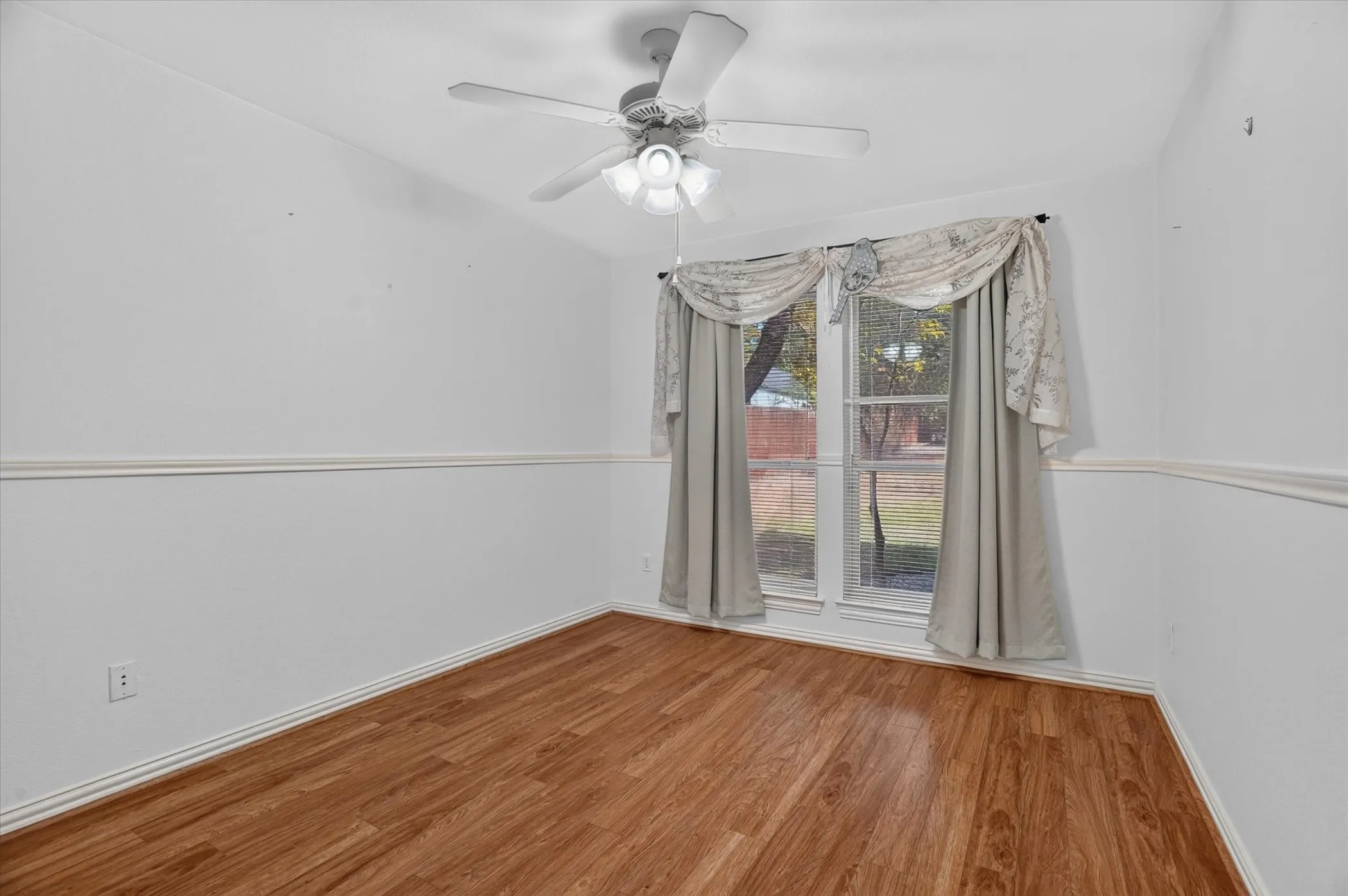 Wood-finish flooring, white walls with decorative trim, and a ceiling fan with integrated lighting