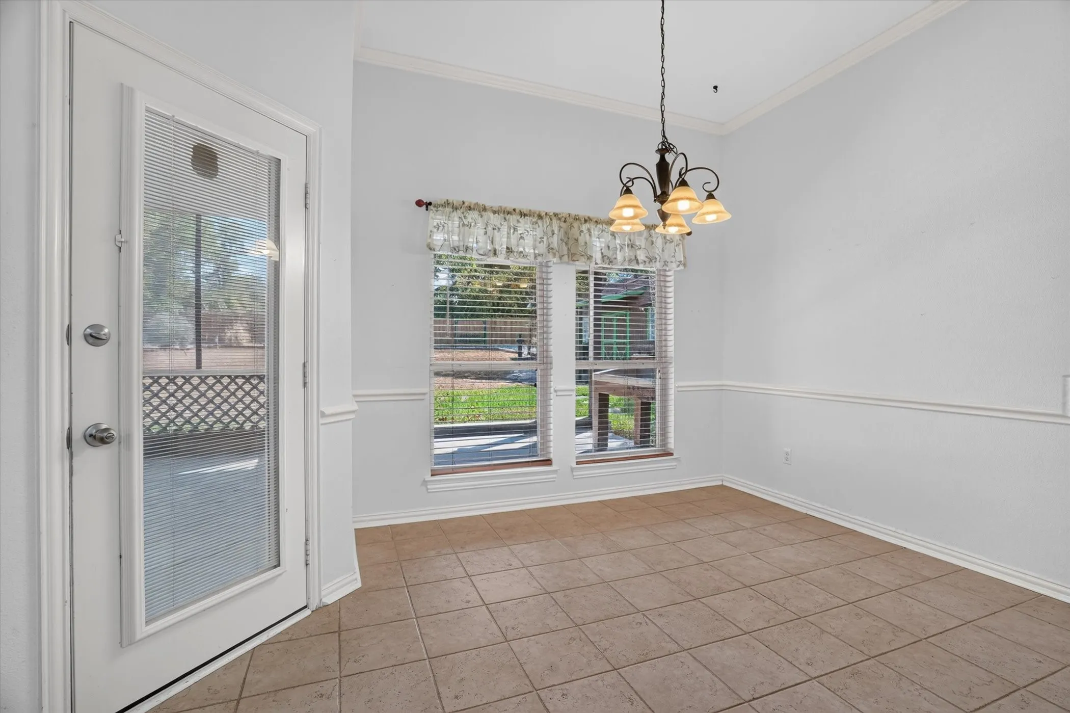 Tile flooring, crown molding, chair rail molding, vaulted ceiling, and a glass-paneled exterior door