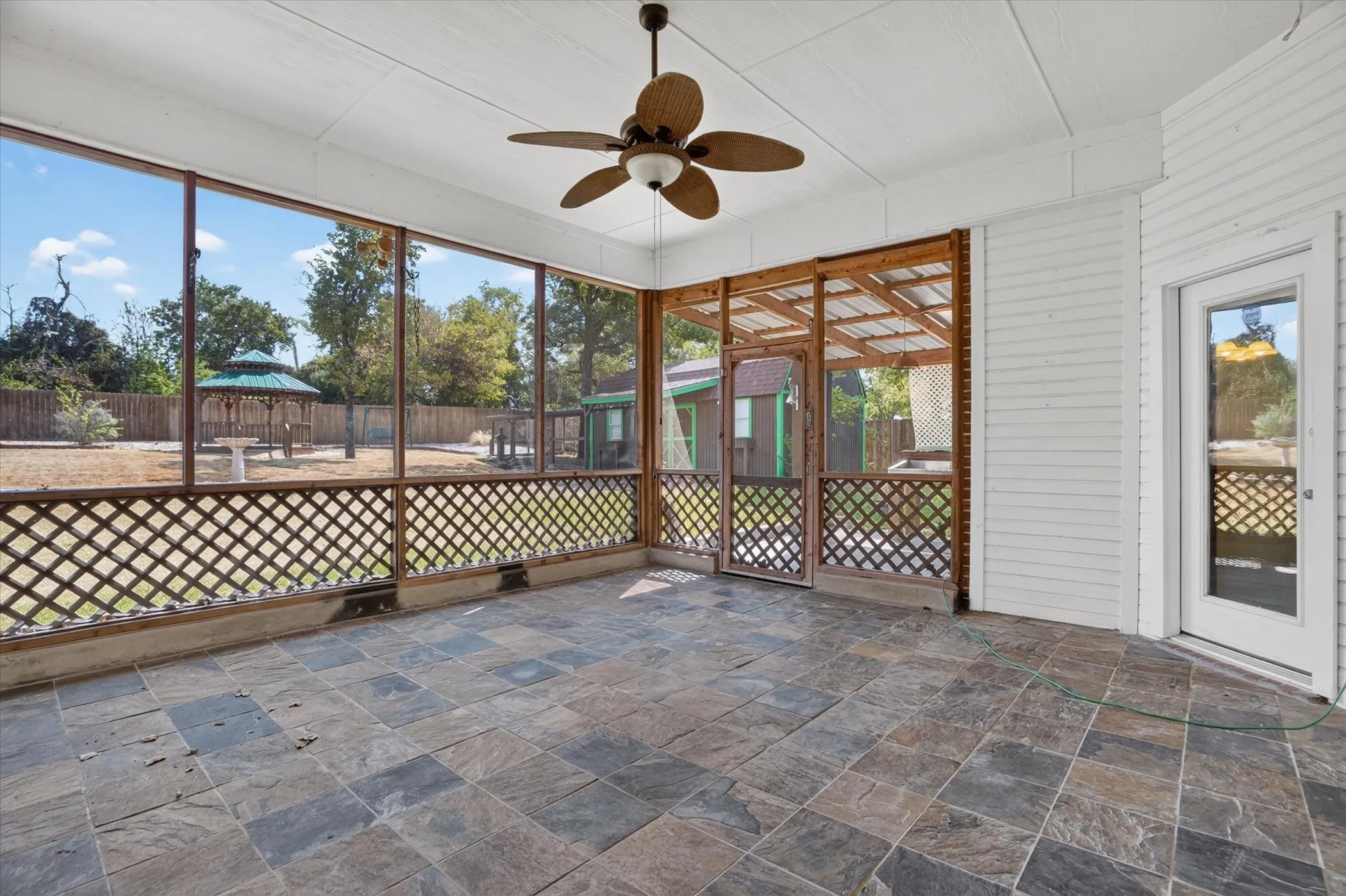Screened porch with natural stone tile flooring, wood lattice detailing, and a ceiling fan