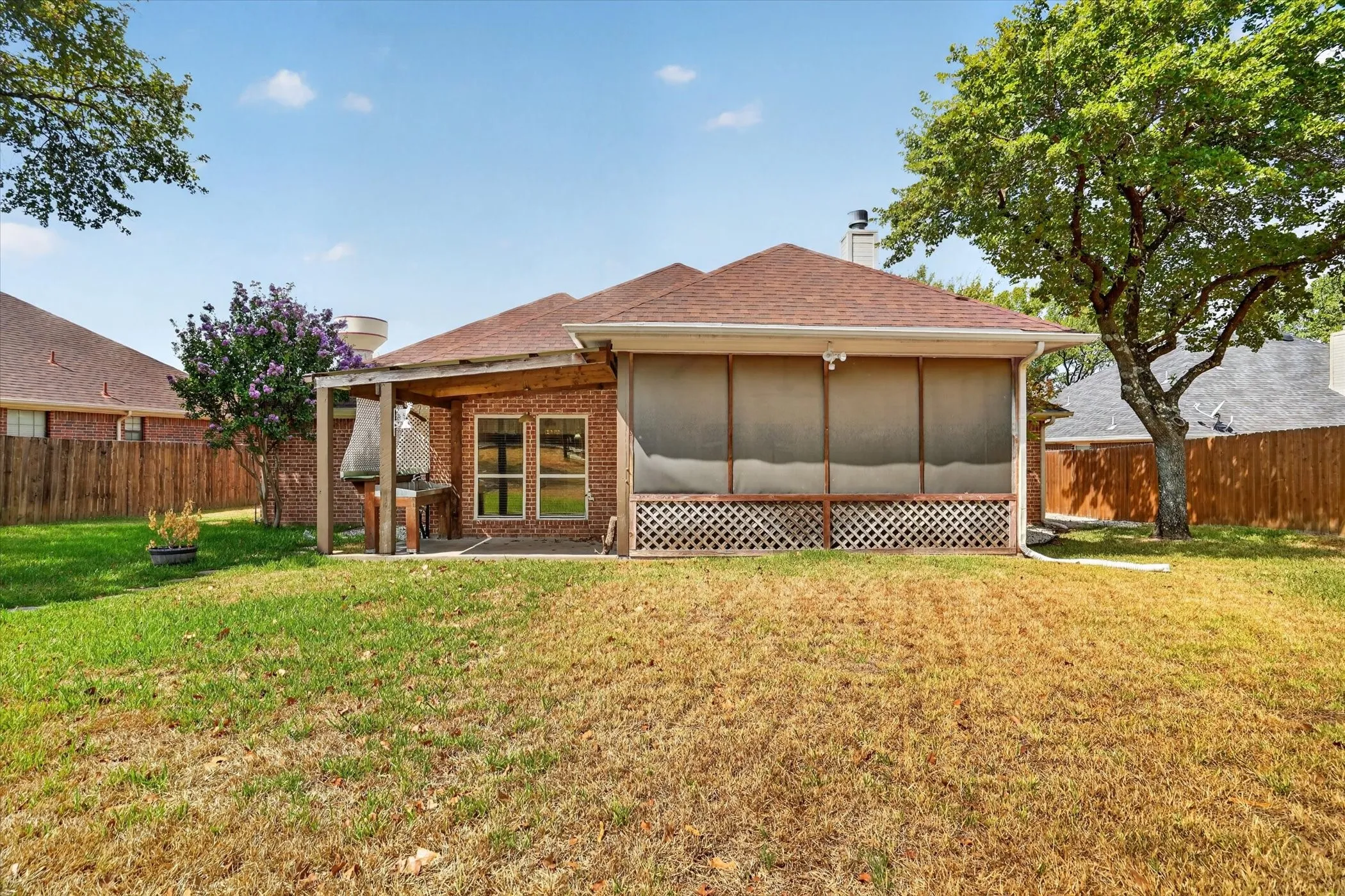 Brick exterior with a covered patio, screened porch, and a mature tree