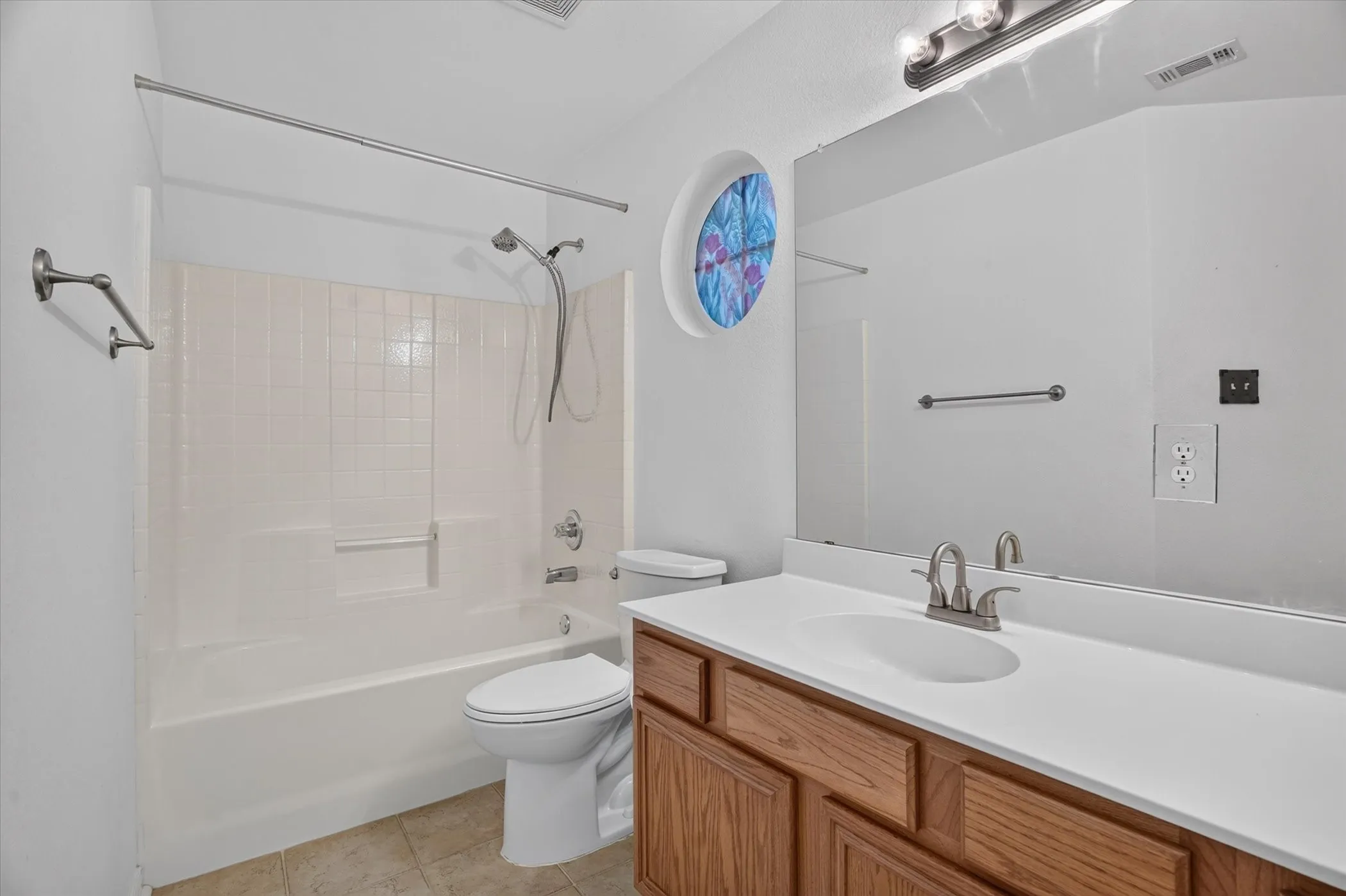 Bathroom featuring a single vanity with wood-finish cabinetry, a large mirror, and a tub with an integrated shower